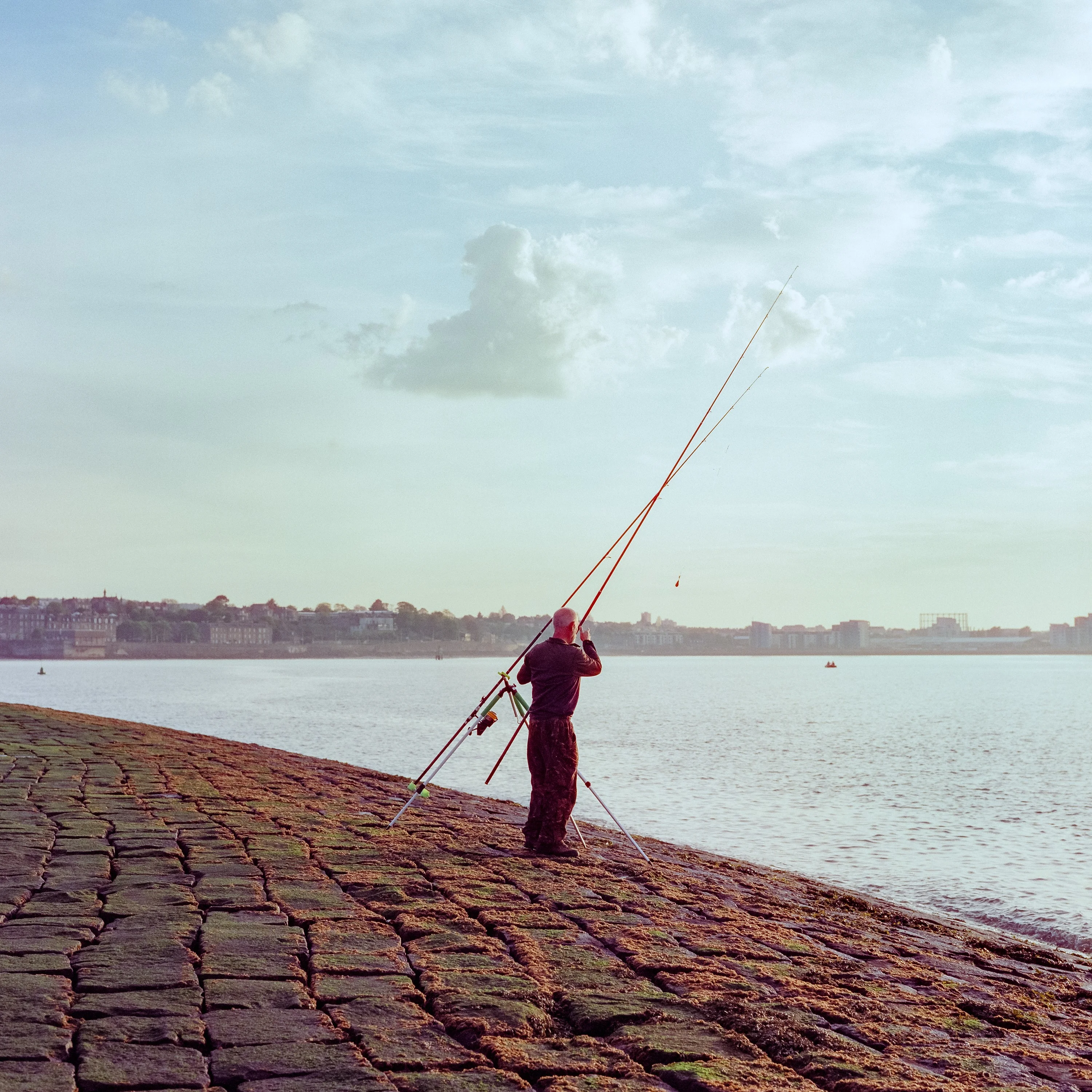 An angler casting a long rod from a cobbled slipway
