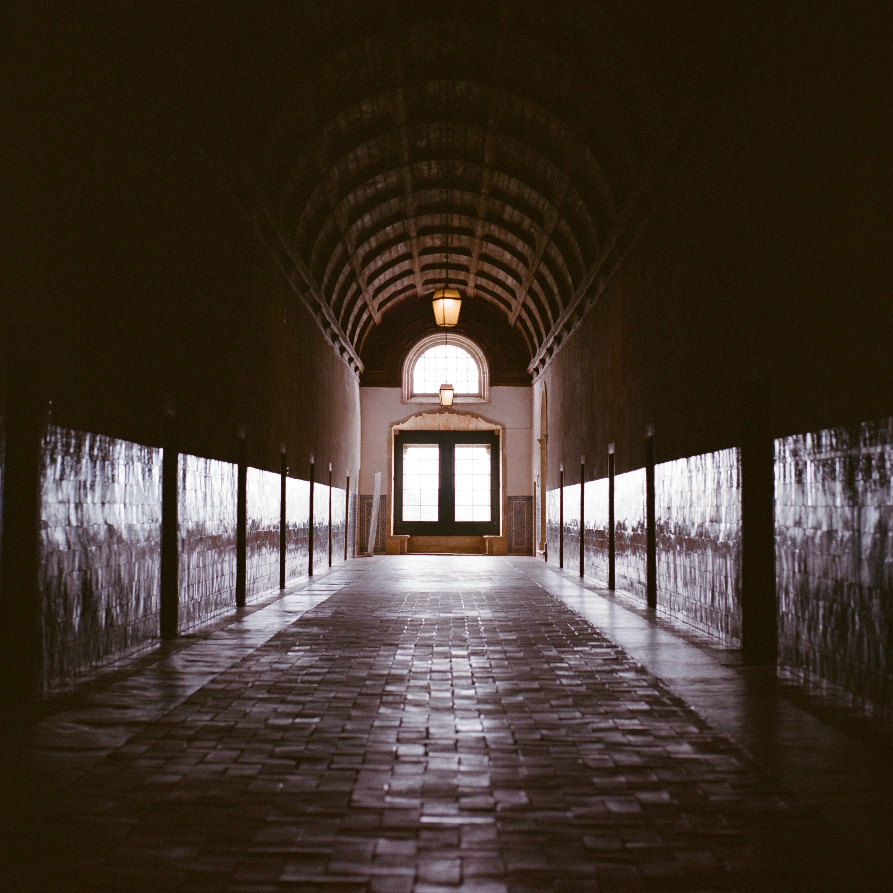 A long vaulted corridor leading to a lit doorway