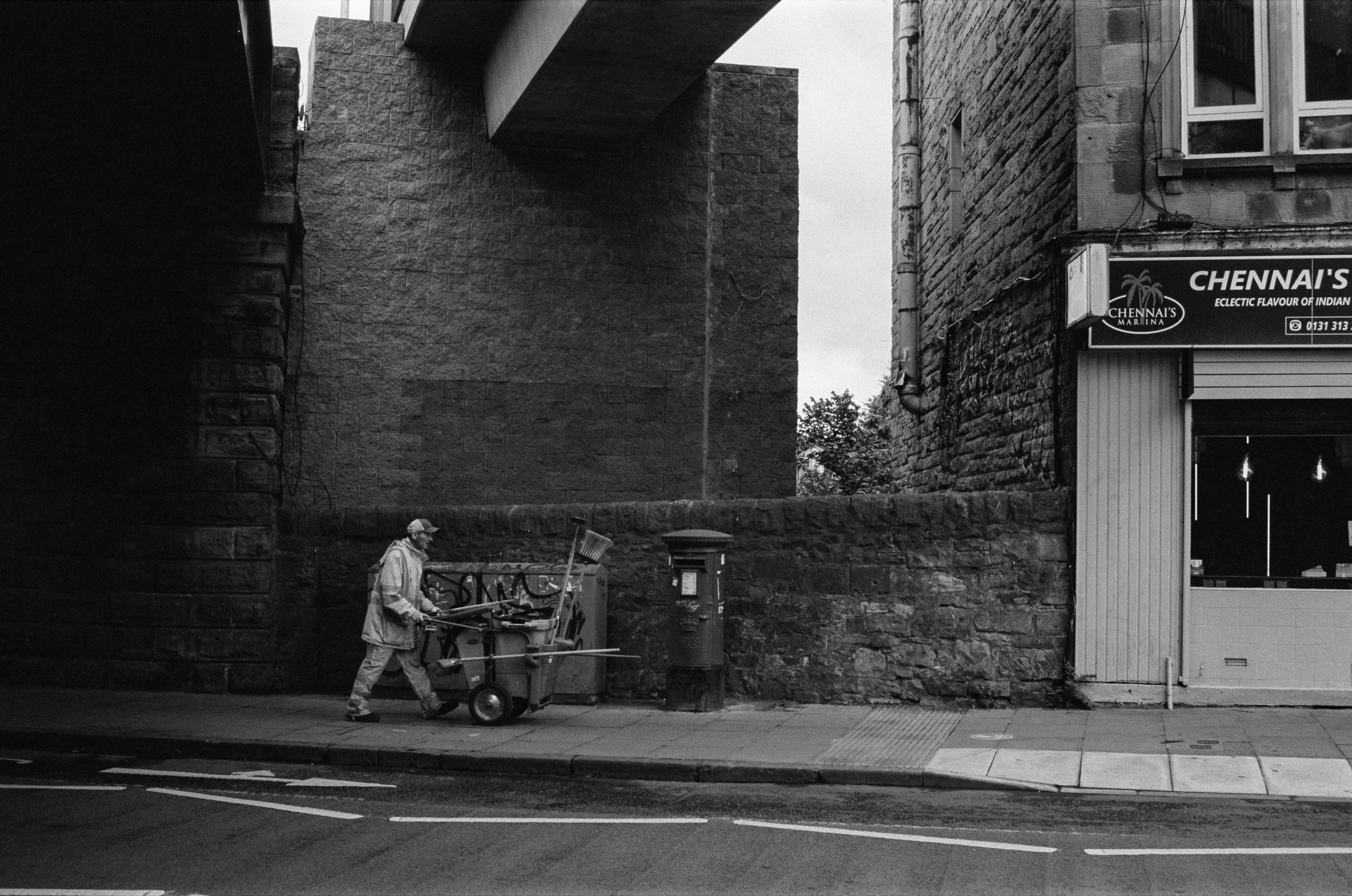 Black and white: a man pushing a barrow under a railway bridge