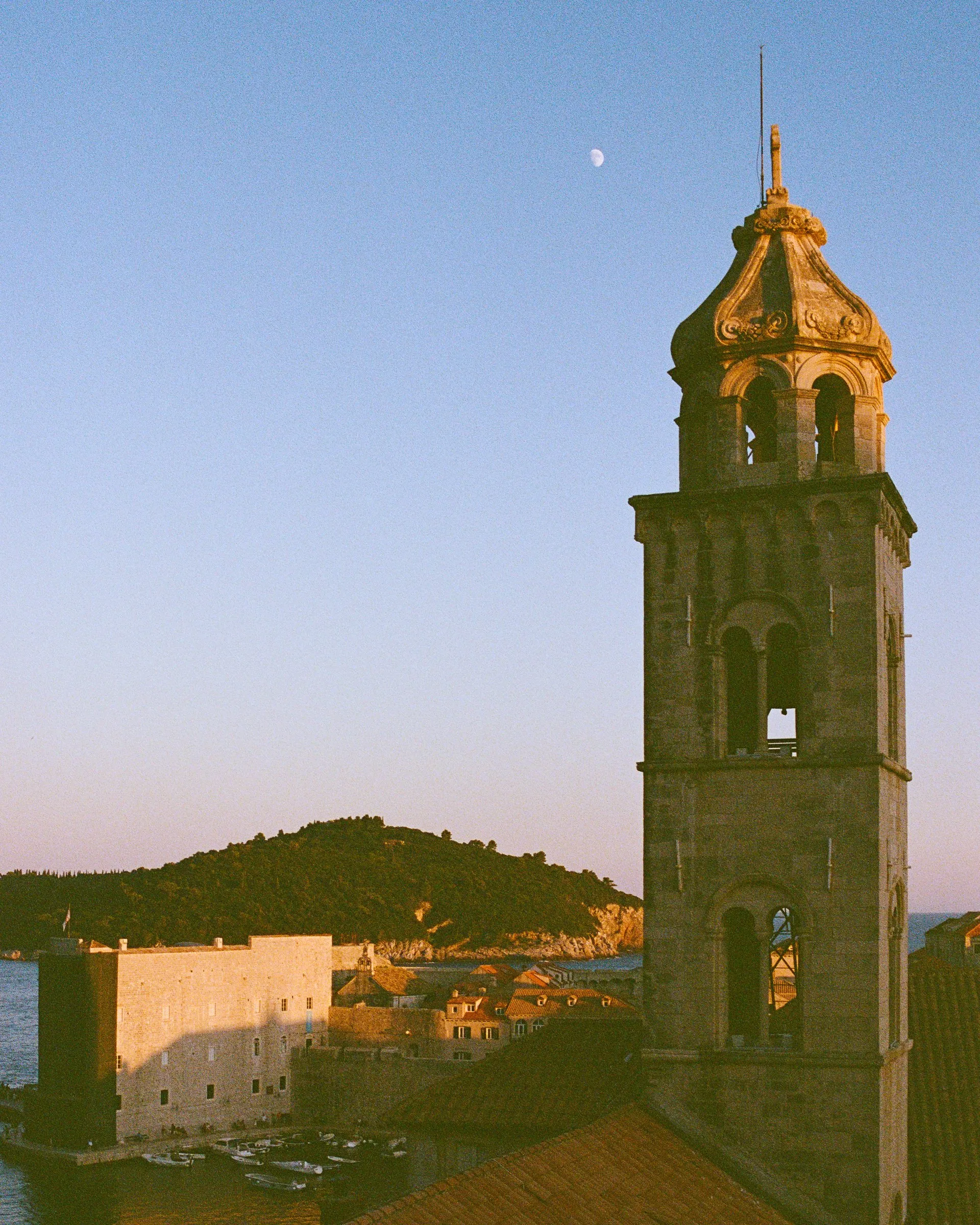 A bell tower against a pale evening sky with the moon above