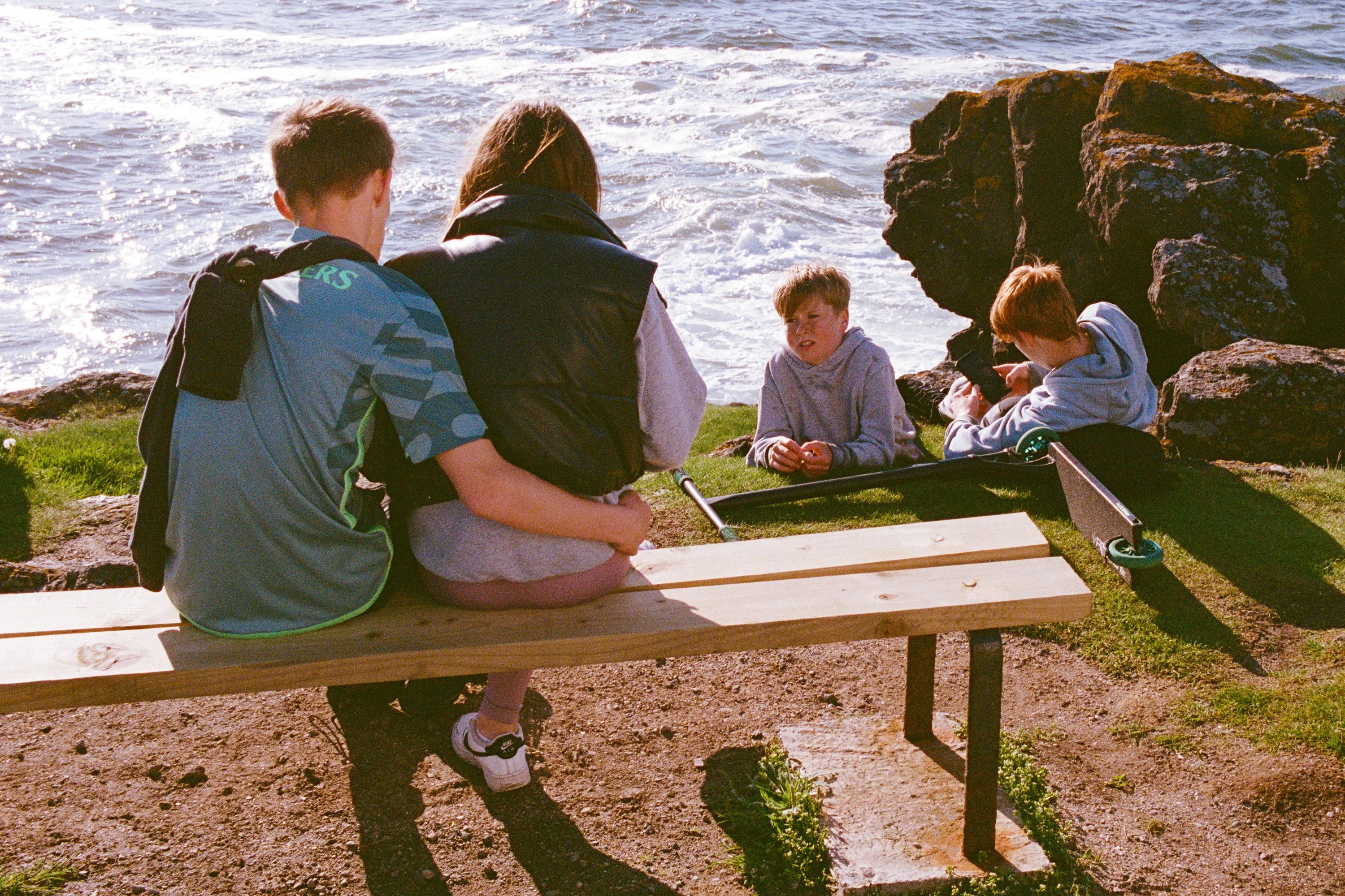 A family on a bench above rocks and surf