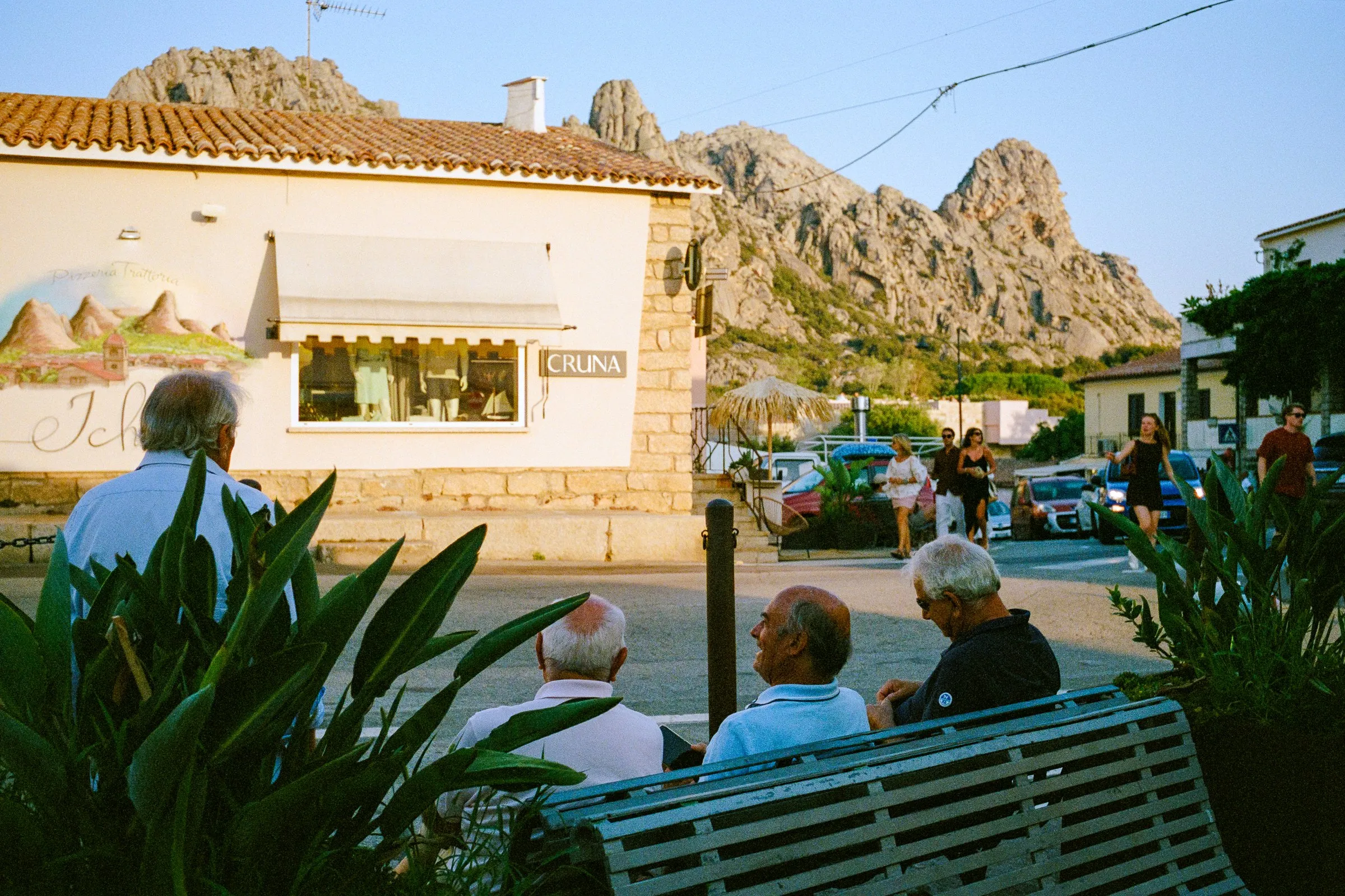 Old men on a bench in the shade, with the village's granite peaks beyond