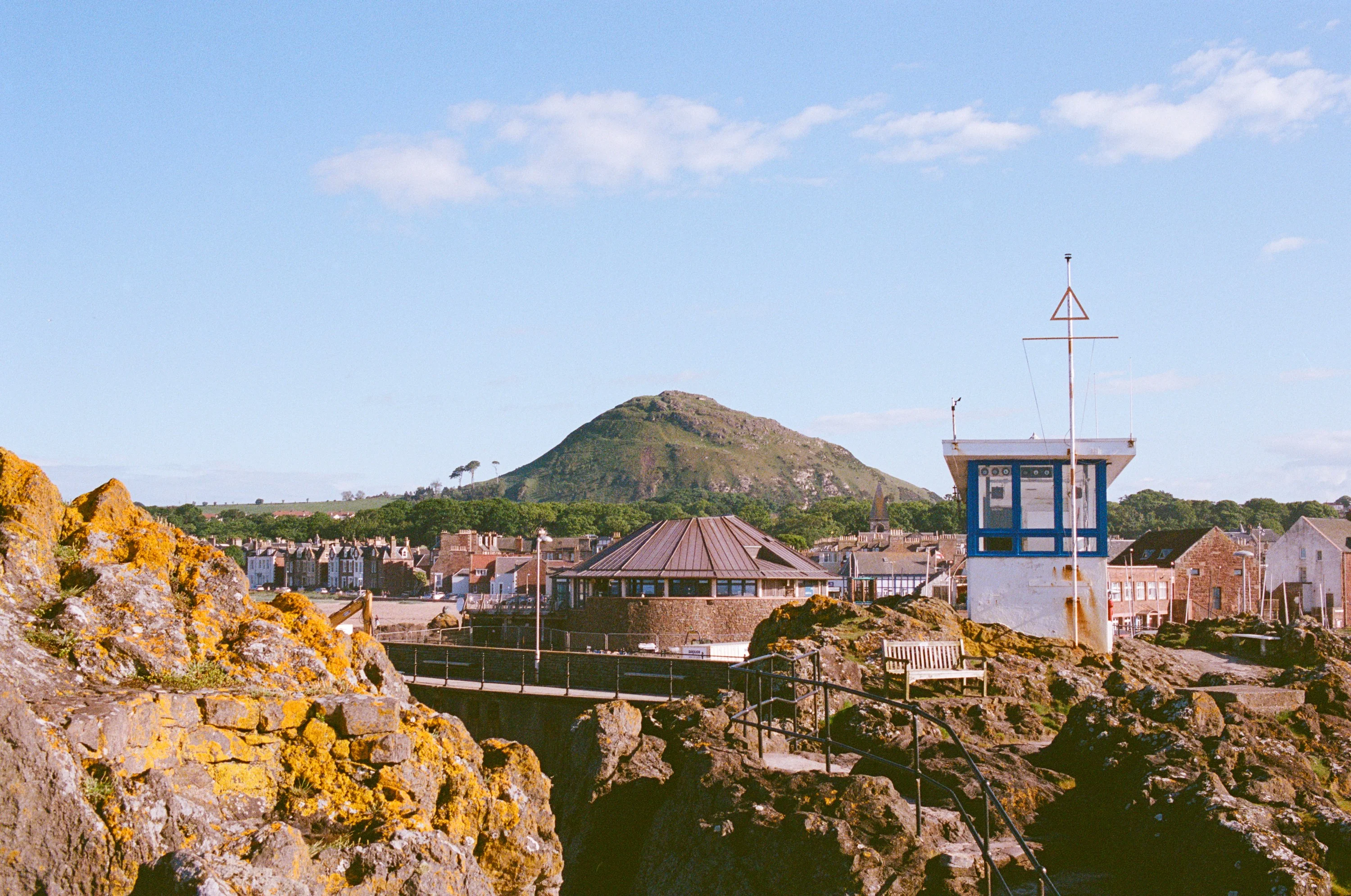 Rocks and a lookout hut in front of a conical hill on the East Lothian coast