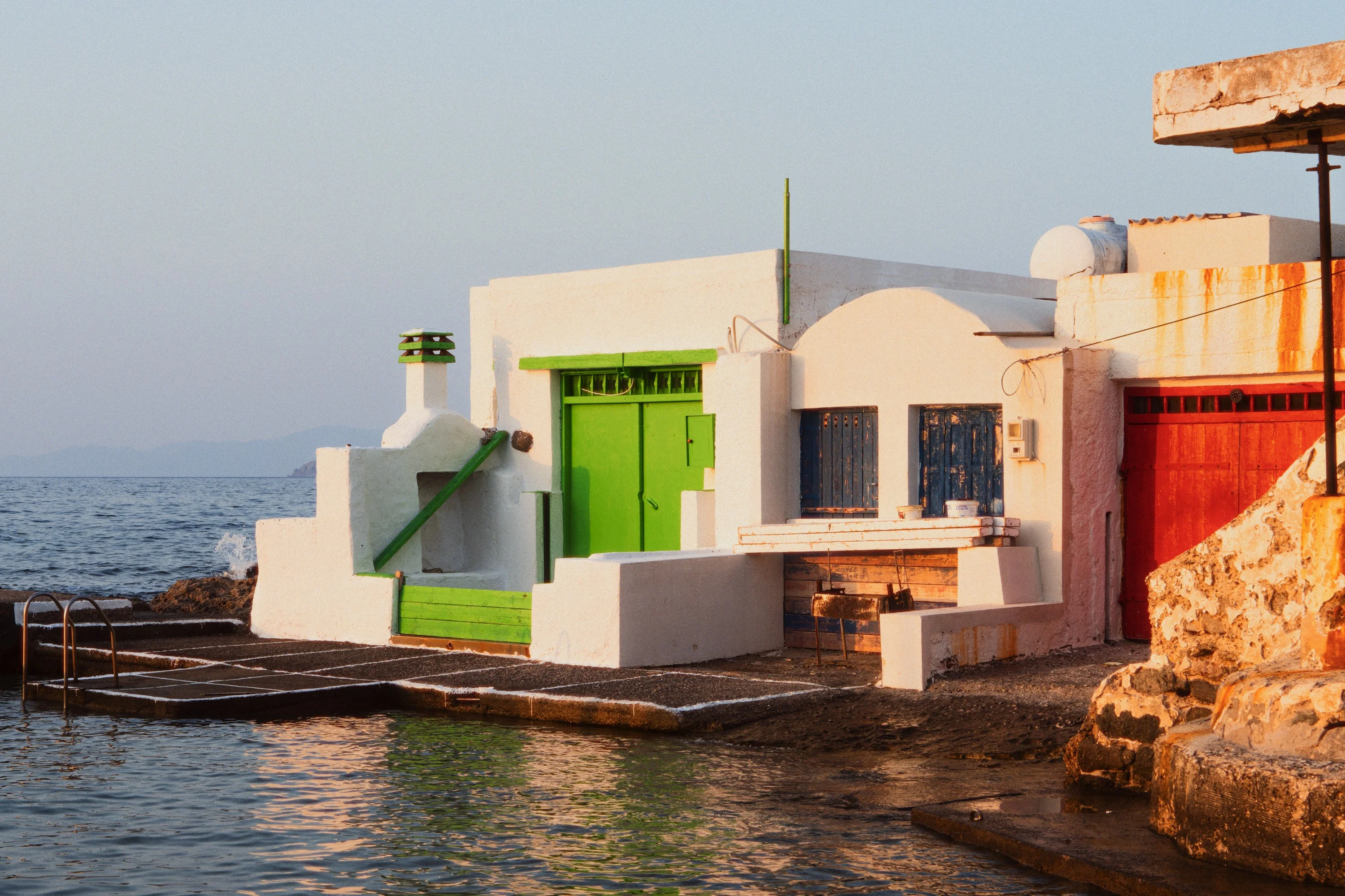 A white boathouse with a green door at the water's edge