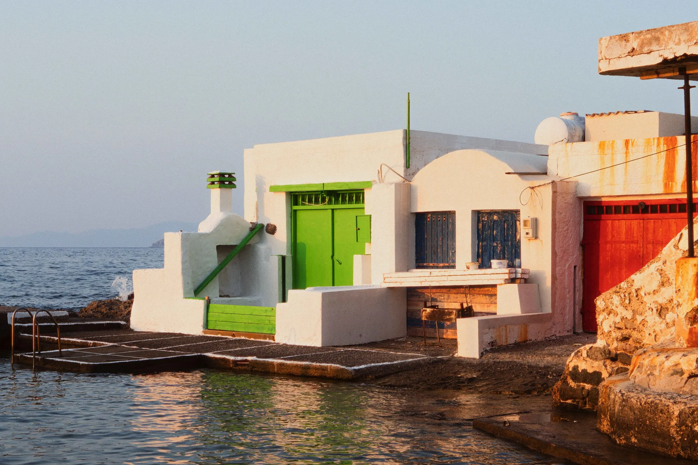 A white boathouse with a green door at the water's edge