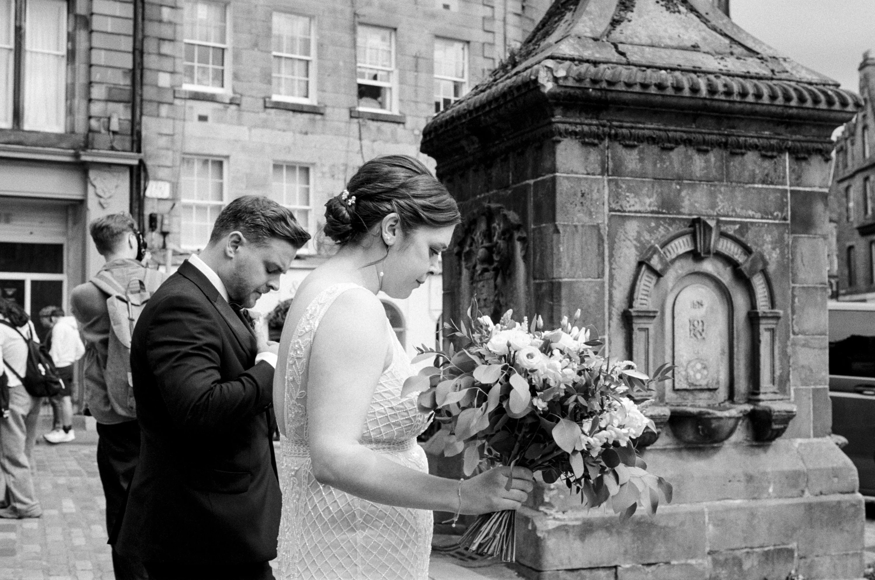 Black and white: a bride and groom with a bouquet by a stone fountain