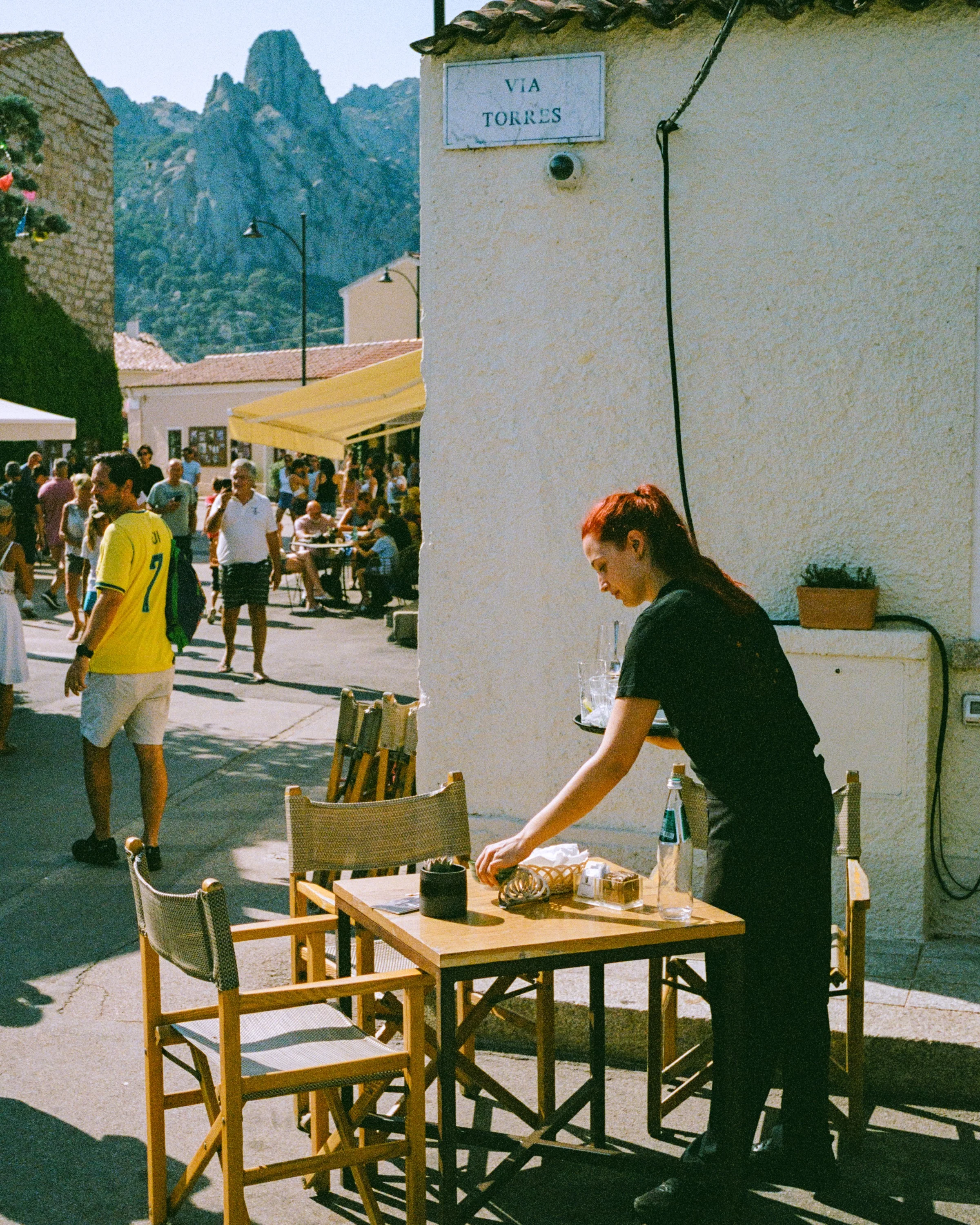A waitress setting a table on a busy street below the peaks