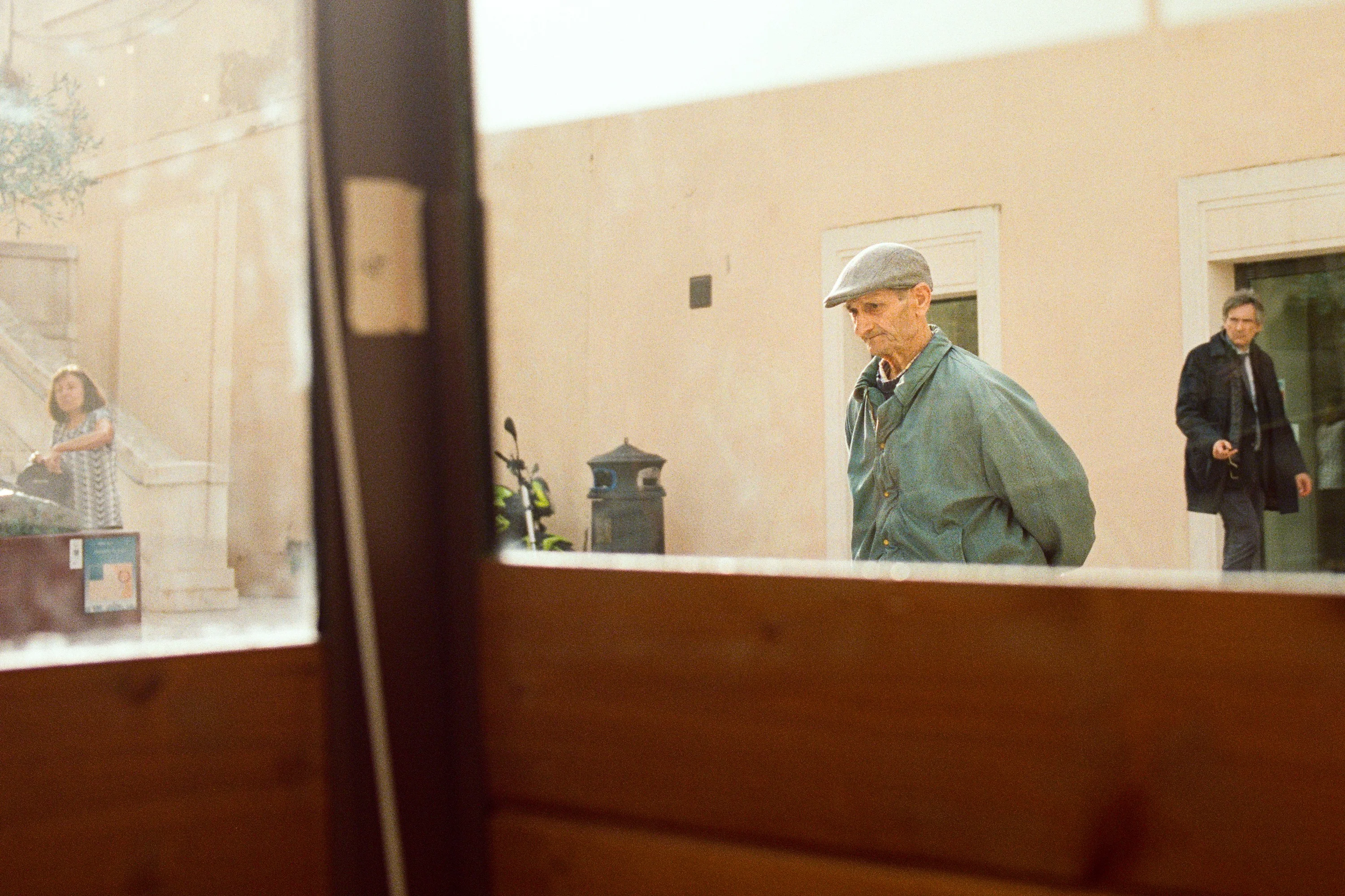 An old man in a flat cap glimpsed through a café window