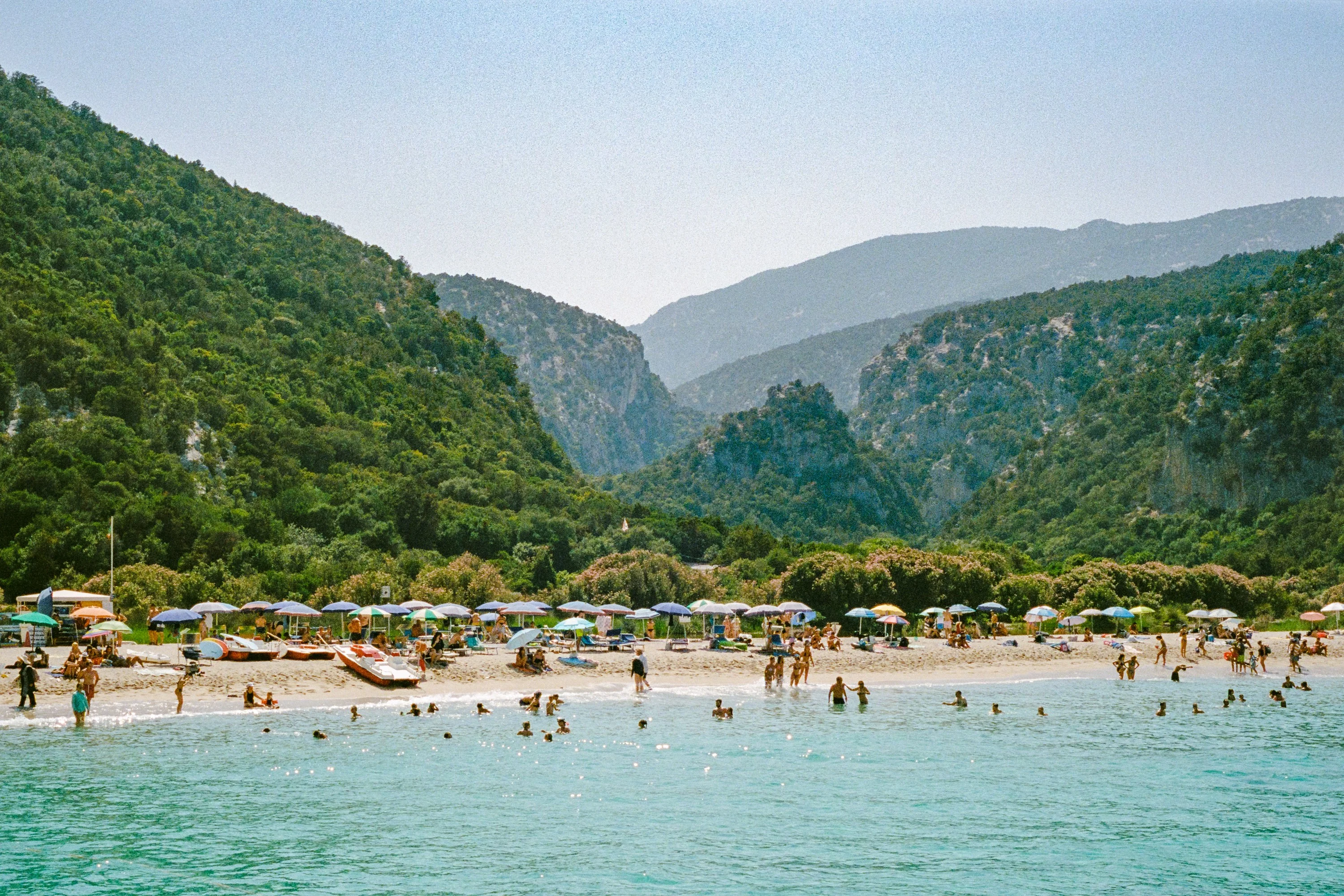 A beach crowded with umbrellas between green valleys