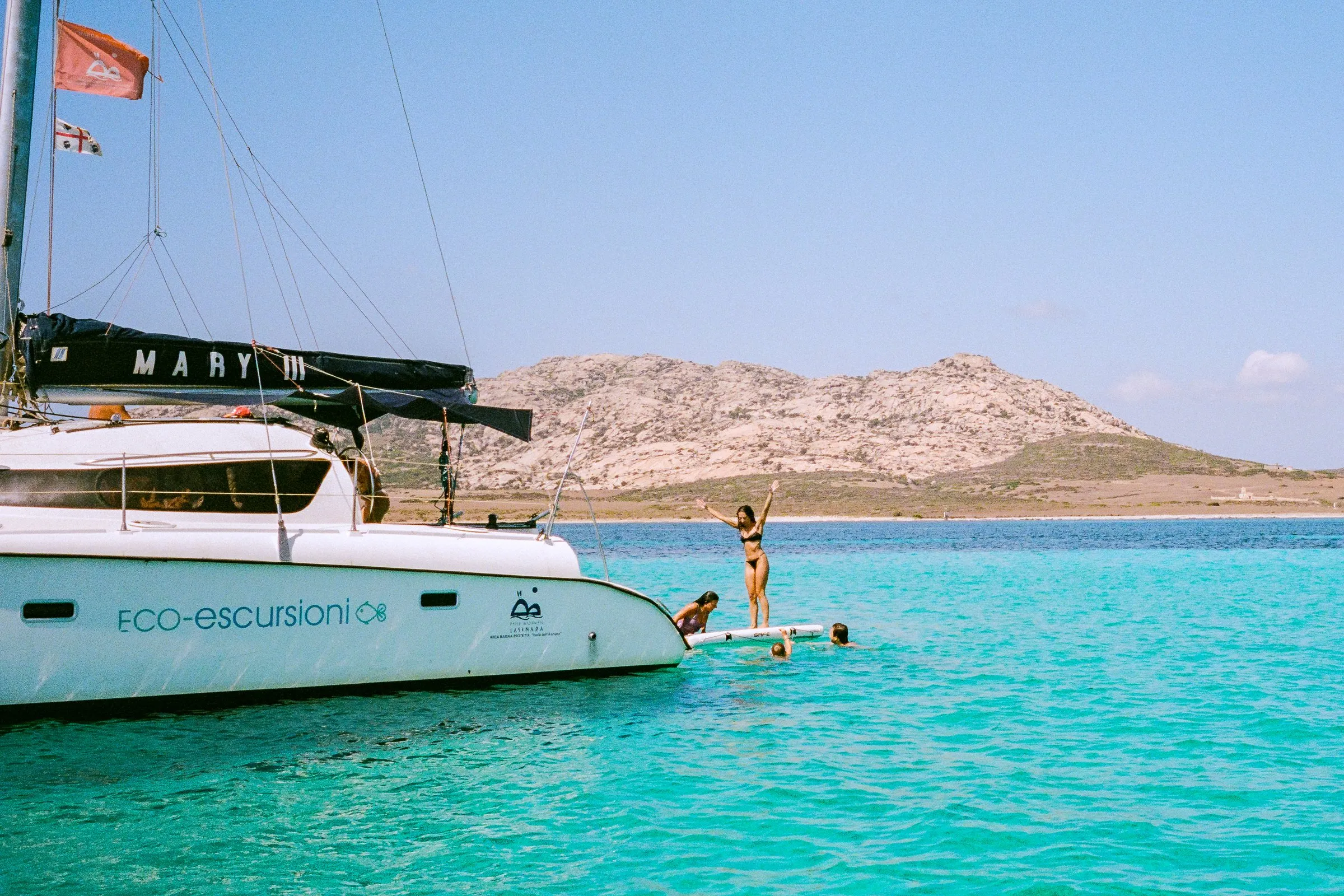 A white catamaran on turquoise water, with a low rocky island behind