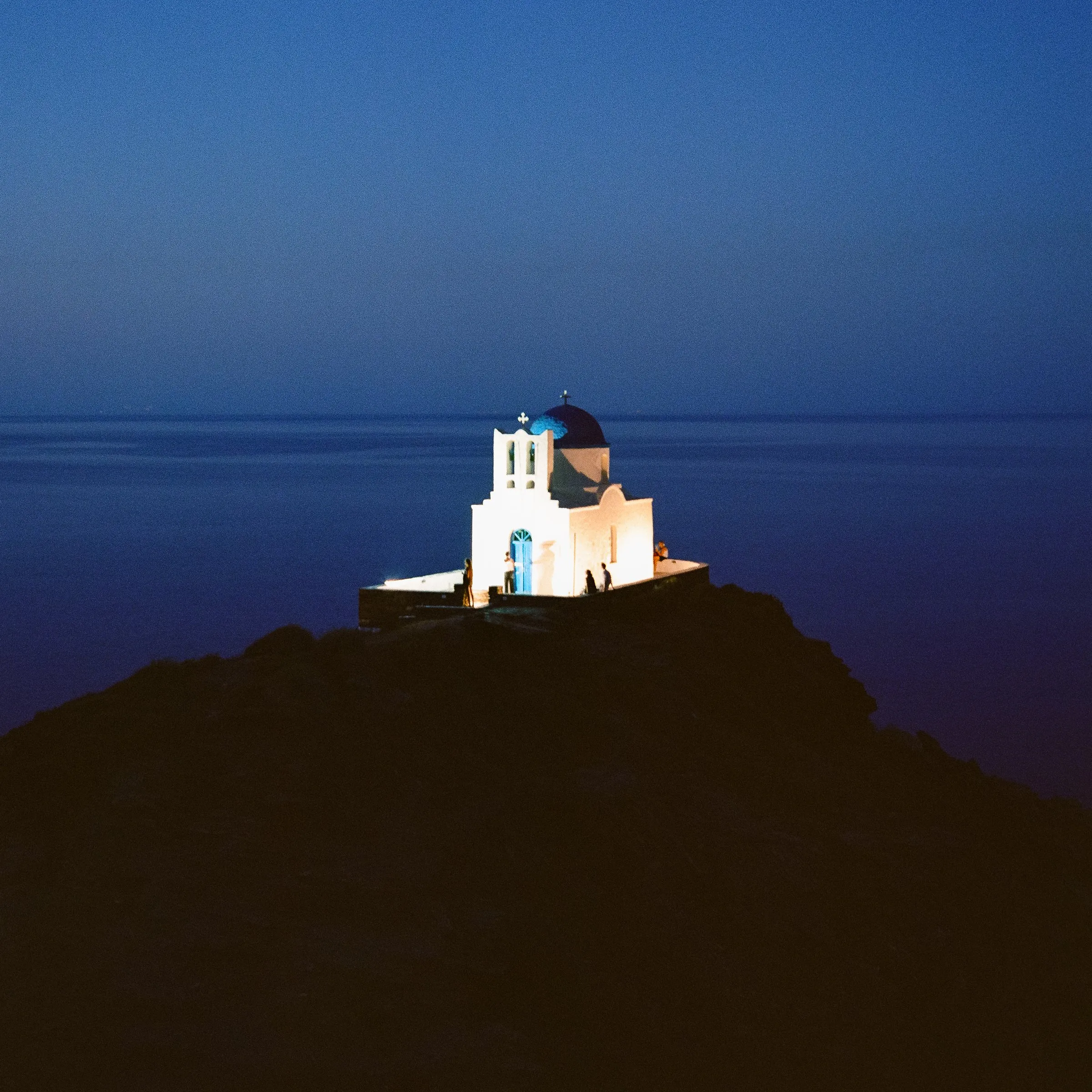 A small white chapel on a rock by the sea at blue hour