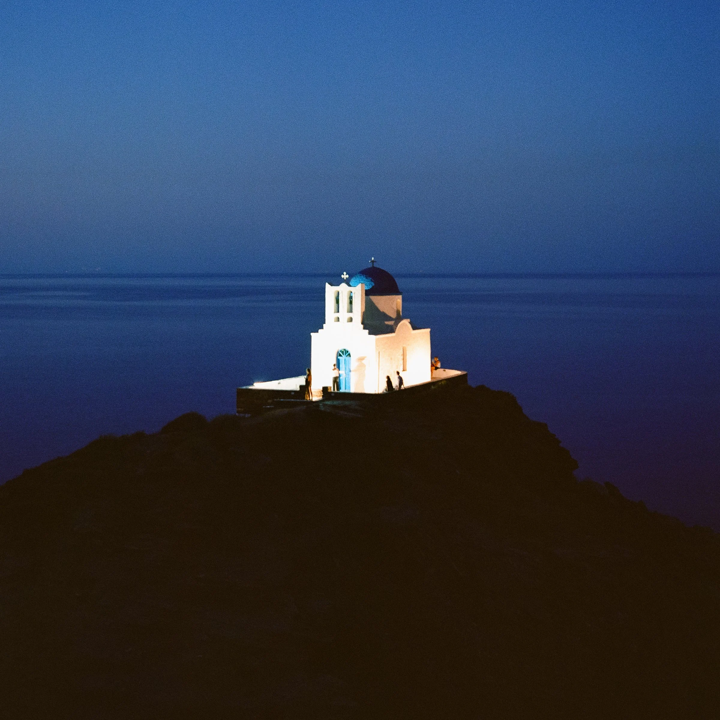 A small white chapel on a rock by the sea at blue hour