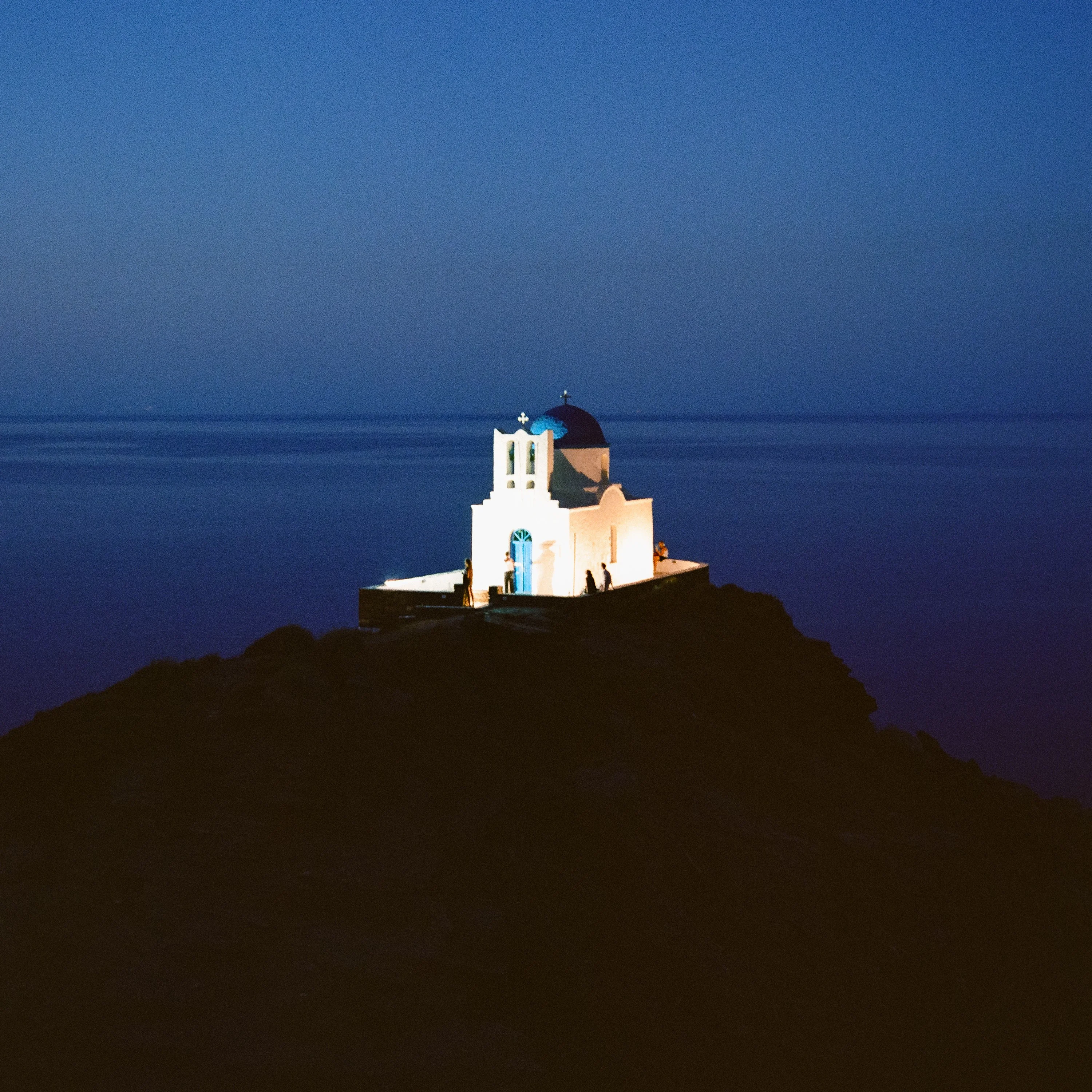 A small white chapel on a rock by the sea at blue hour