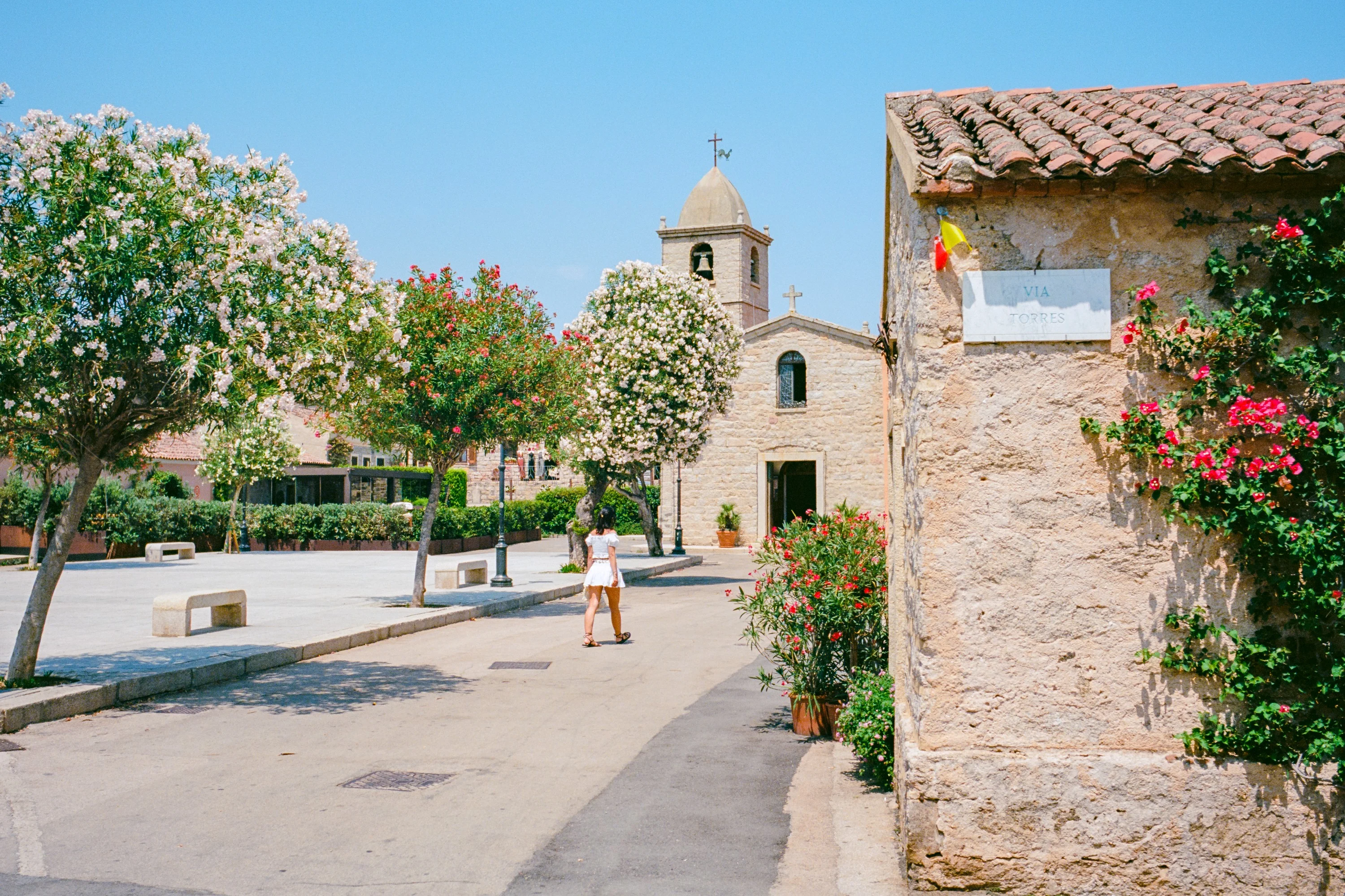 A small square with a stone church and oleanders