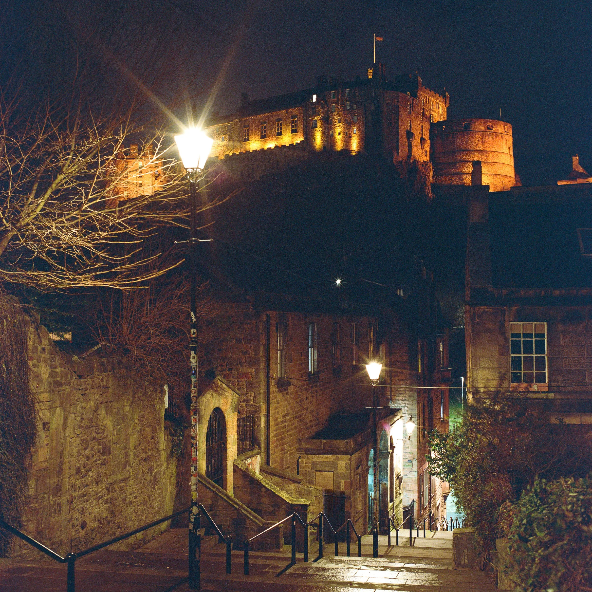A narrow Old Town close at night with the castle lit above