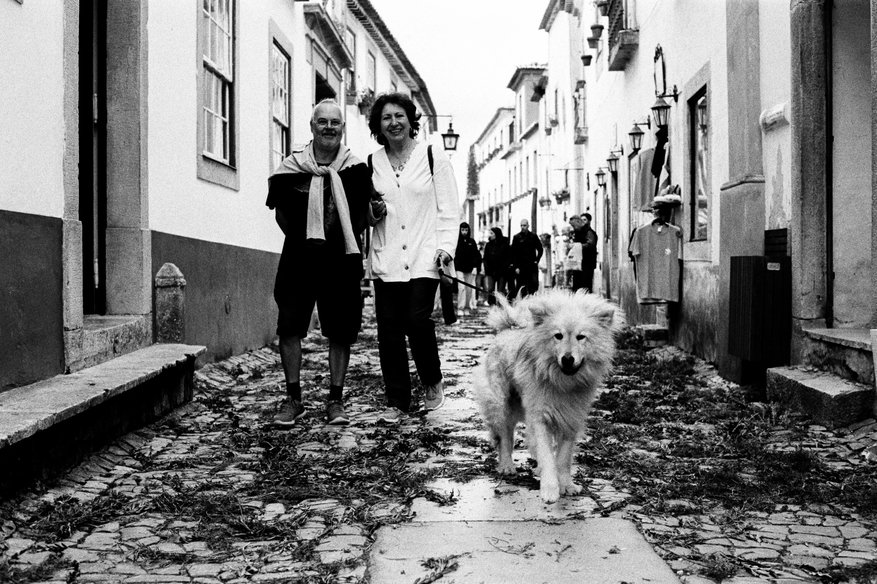Black and white: a couple and a white dog on a cobbled street