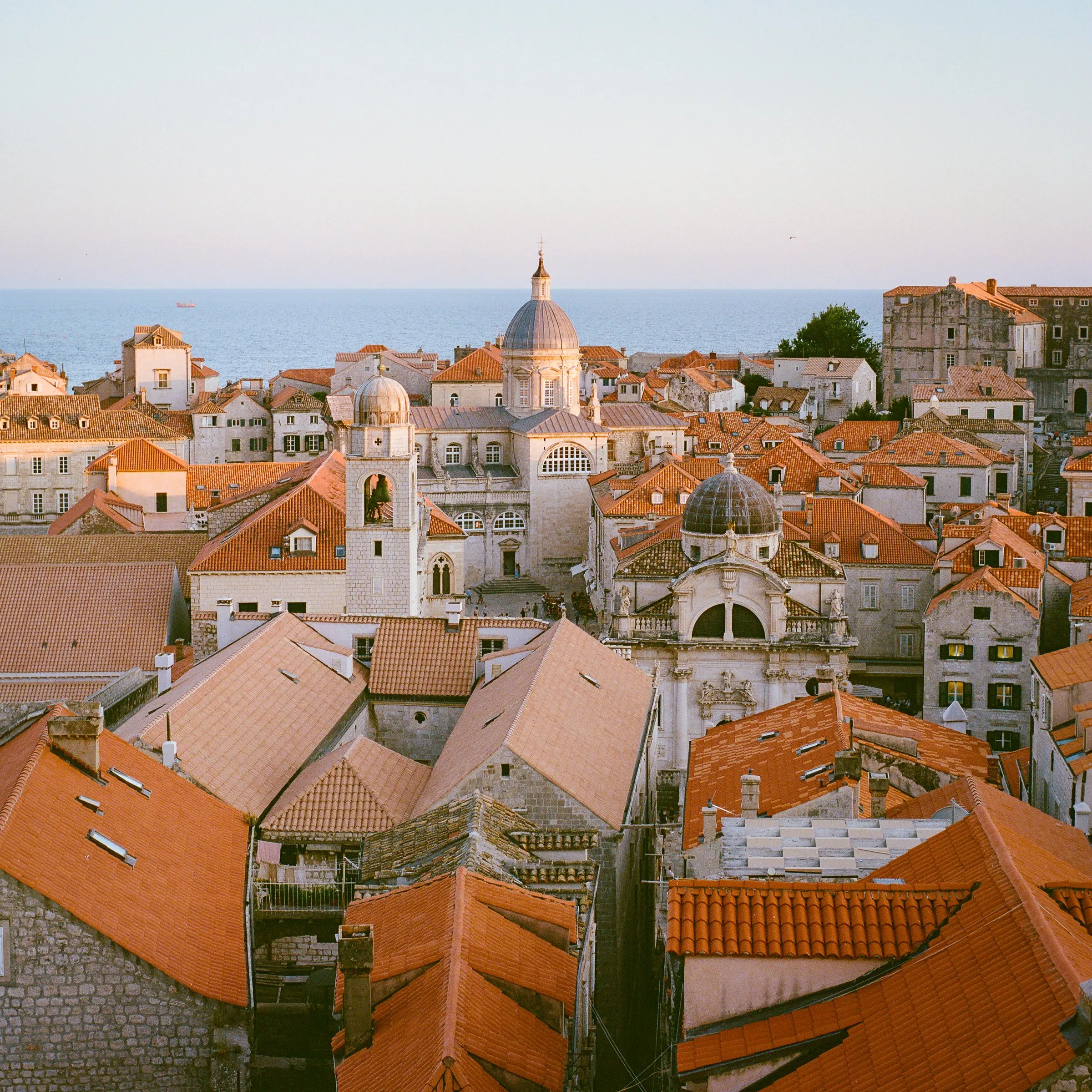 Terracotta rooftops and domes of Dubrovnik's old town, the sea beyond in evening light