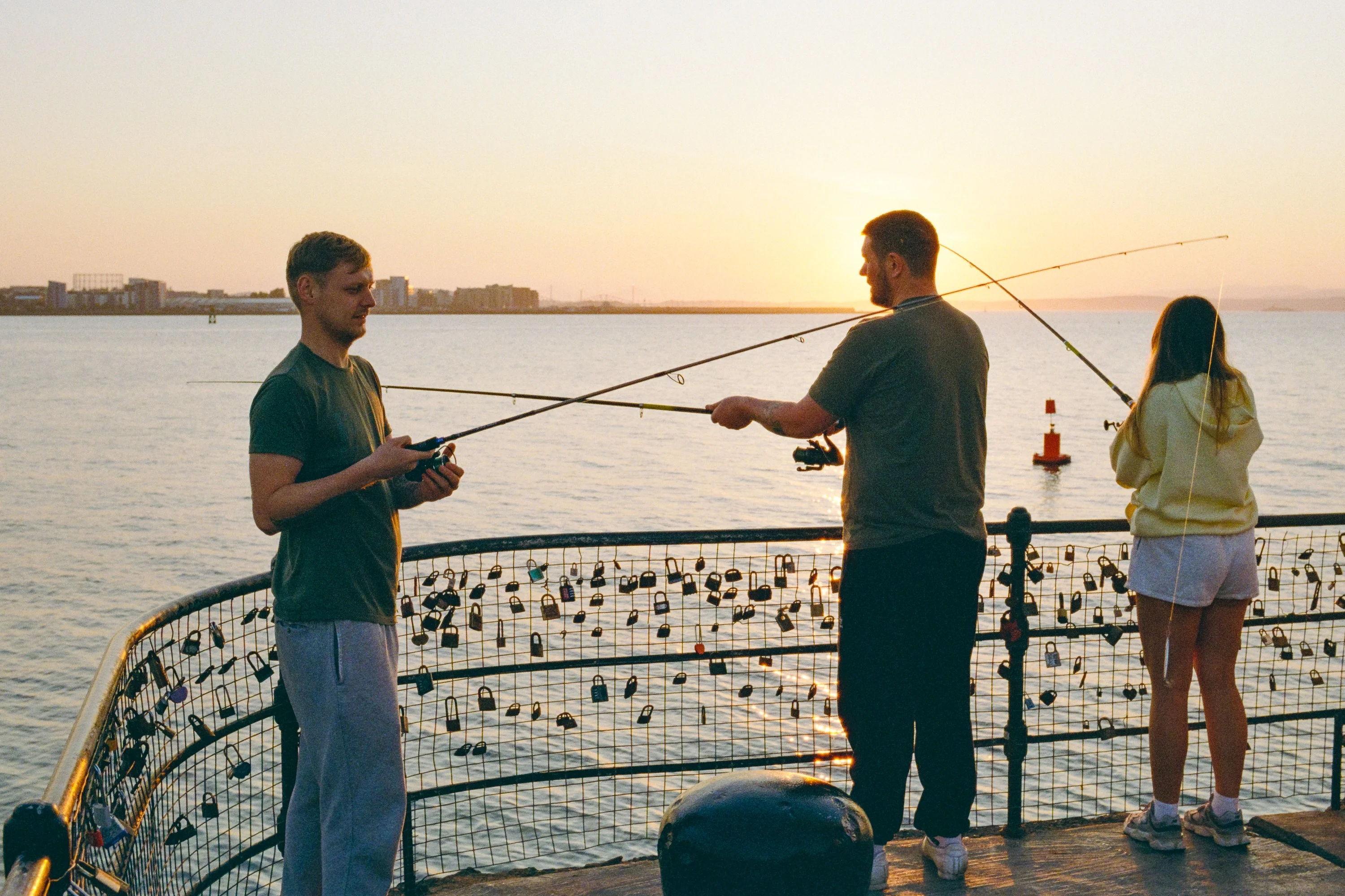 Men fishing from the railings at sunset, a woman watching