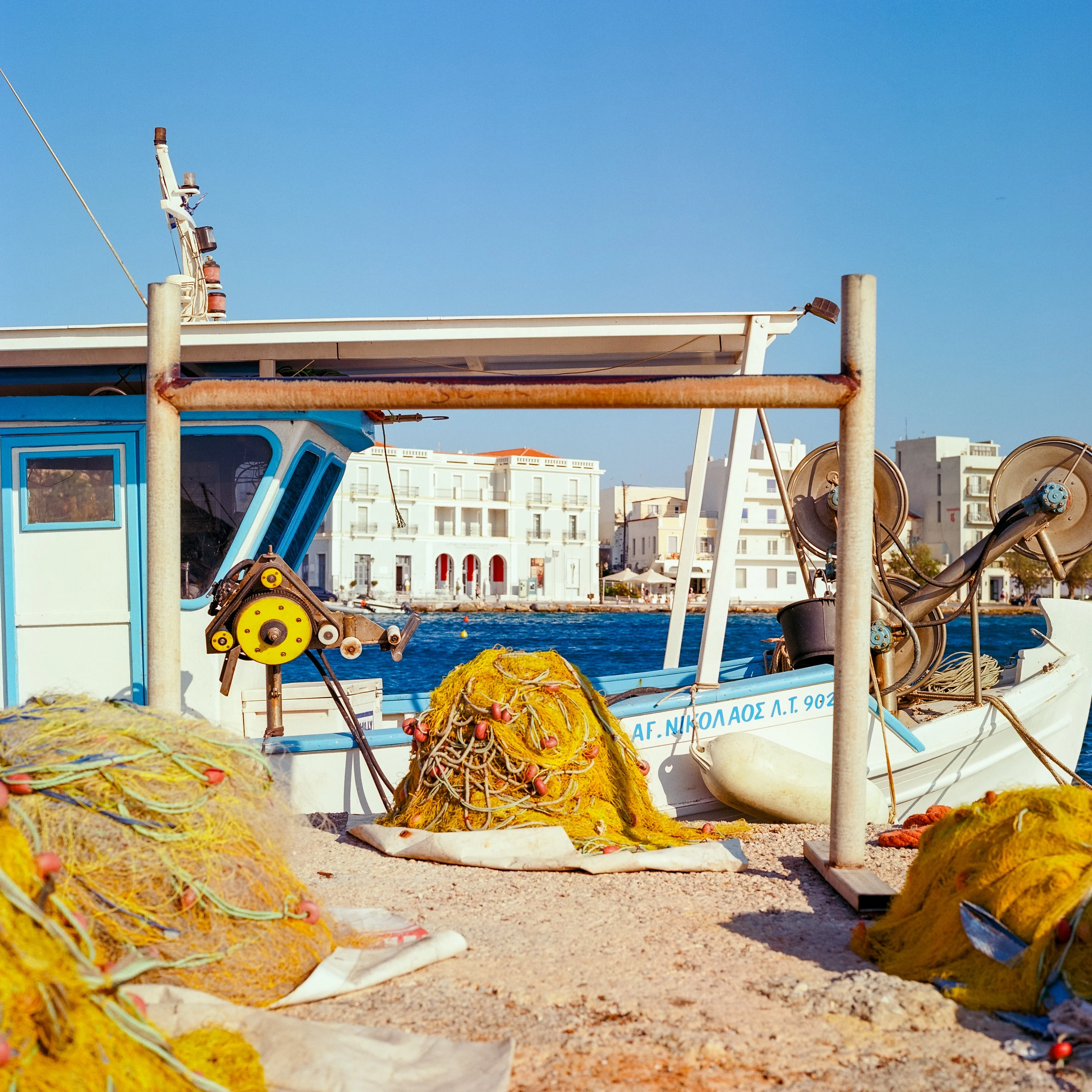 Yellow fishing nets heaped on a quay beside a moored boat, a neoclassical town behind