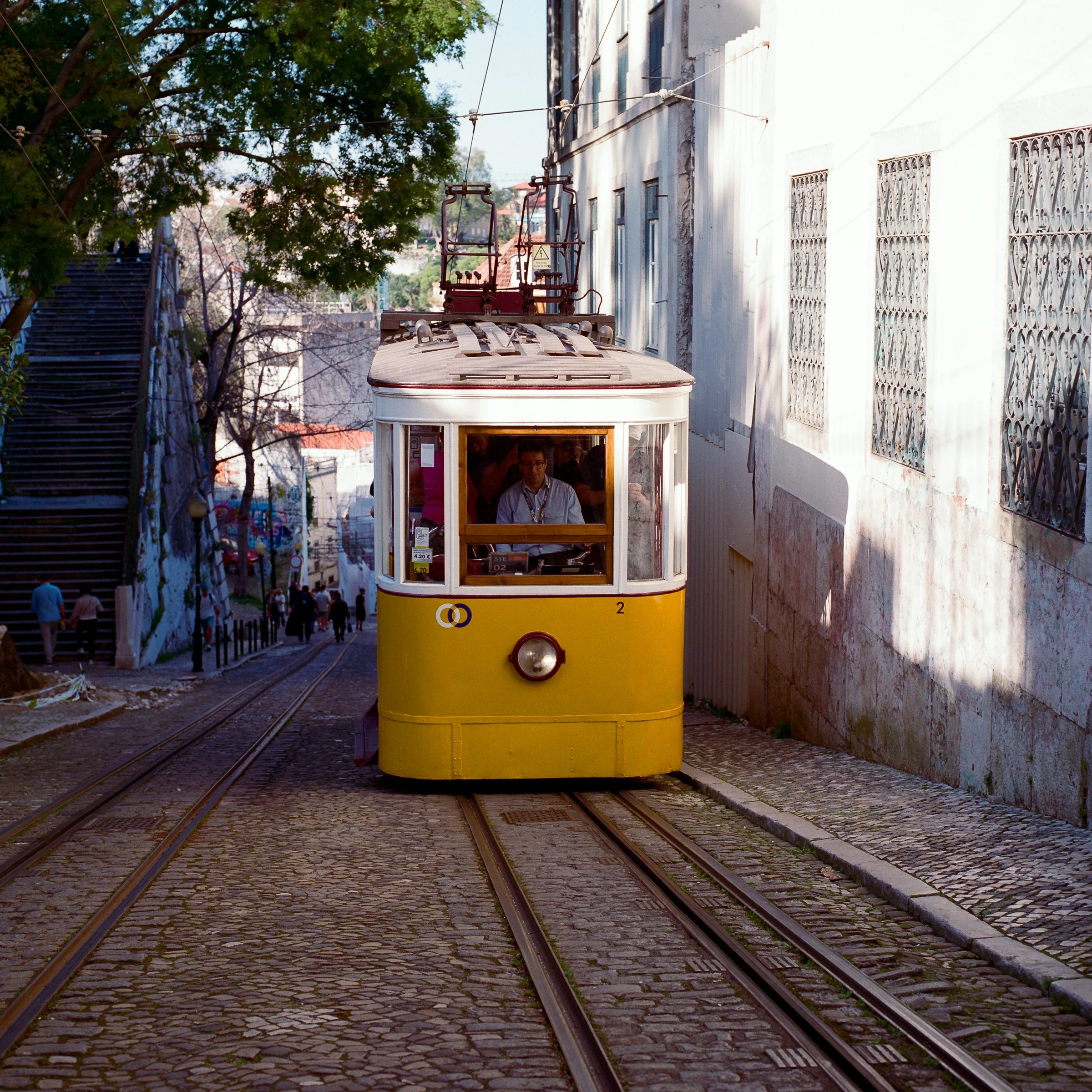 A yellow funicular climbing a steep Lisbon street