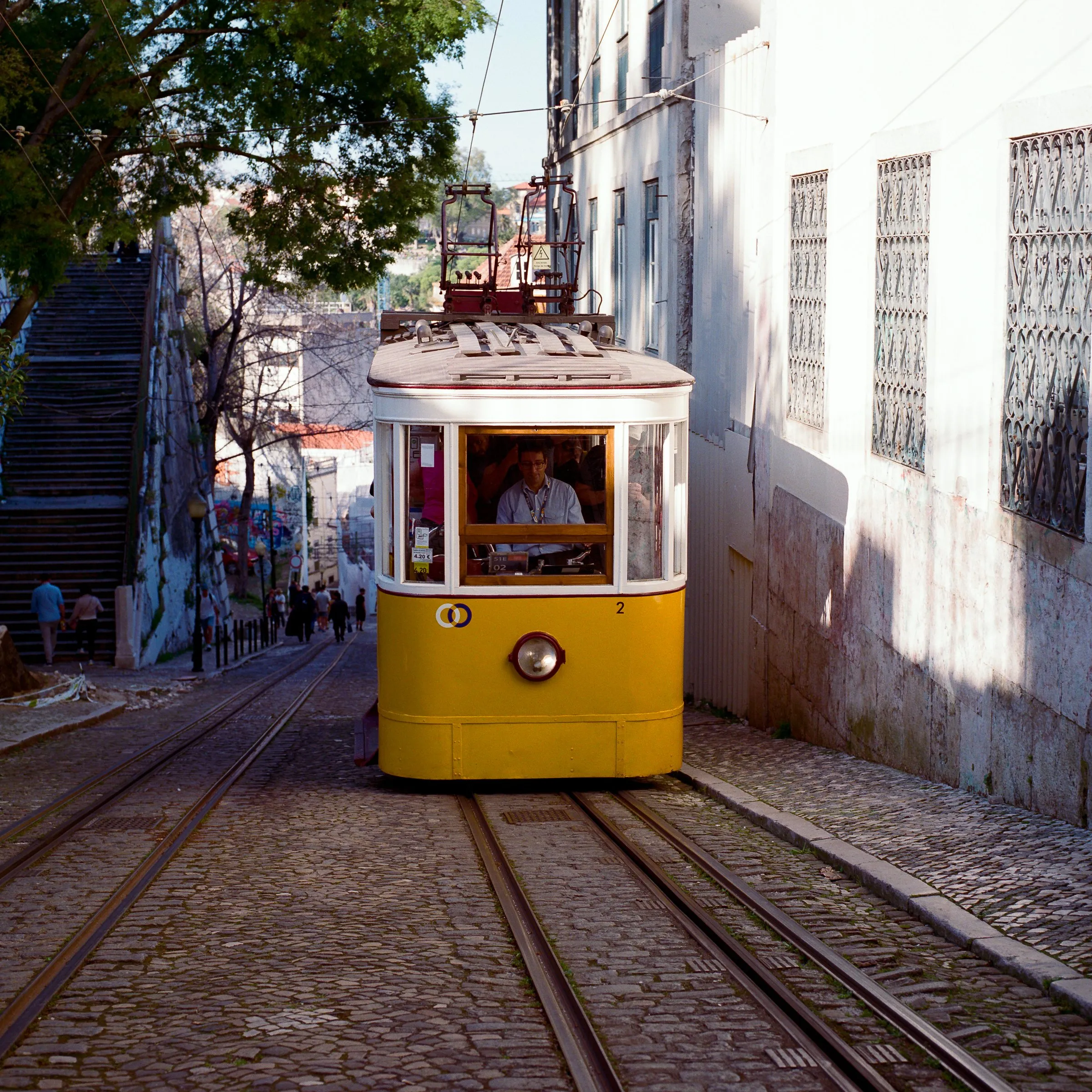 A yellow funicular climbing a steep Lisbon street