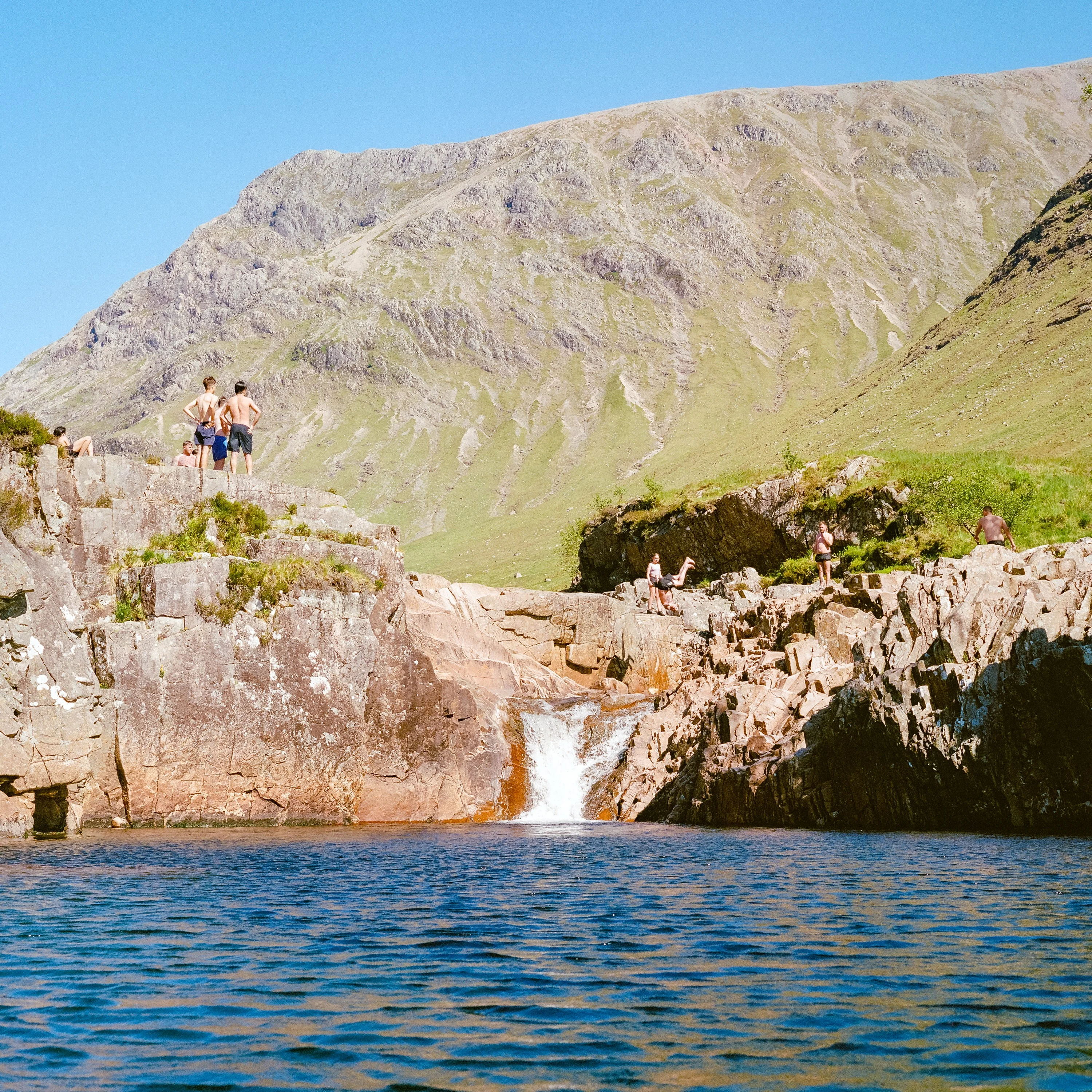 Swimmers on rocks above a pool and waterfall in Glen Etive