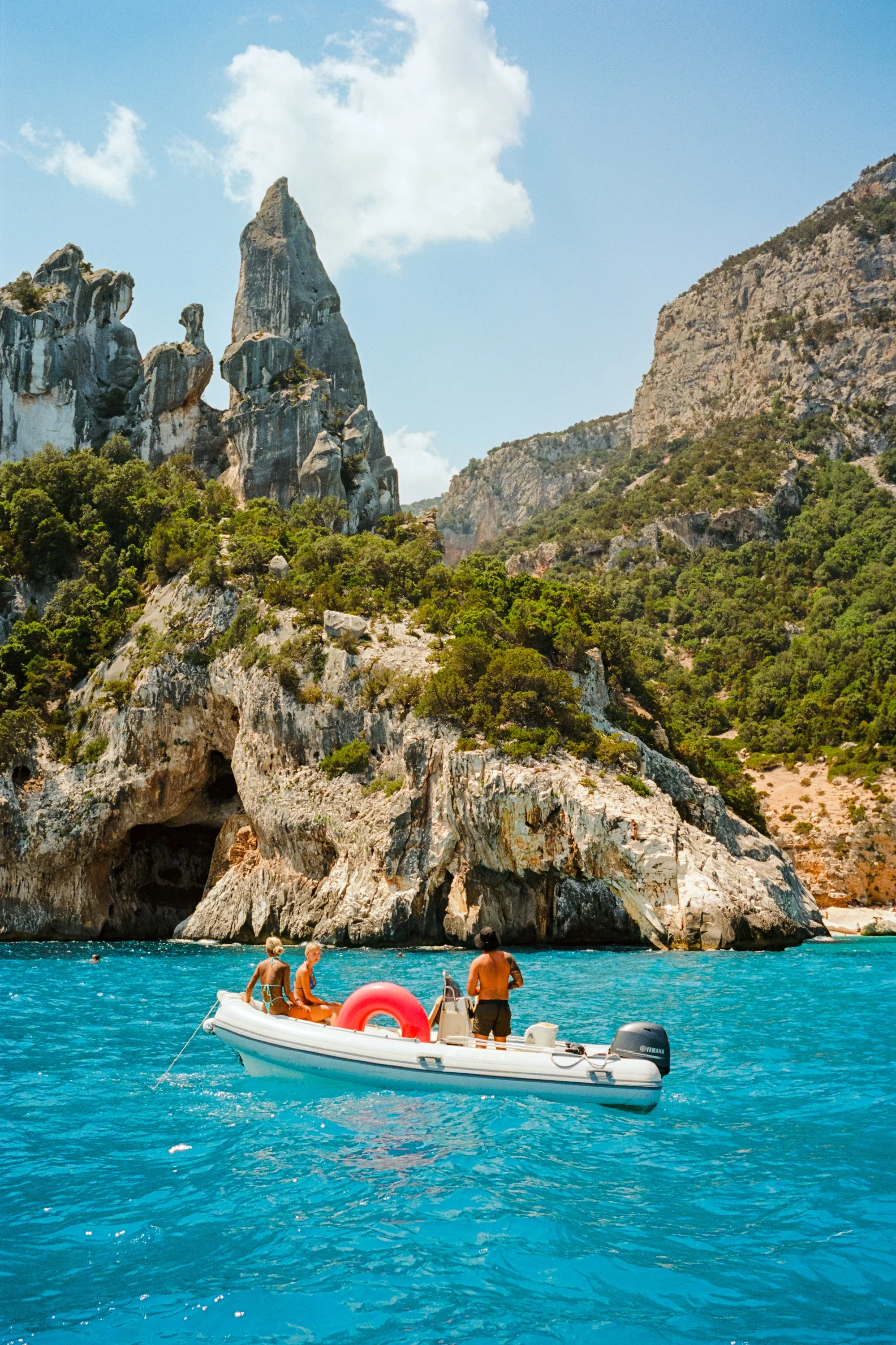 A dinghy floats in bright blue water below the limestone spire of Cala Goloritzé