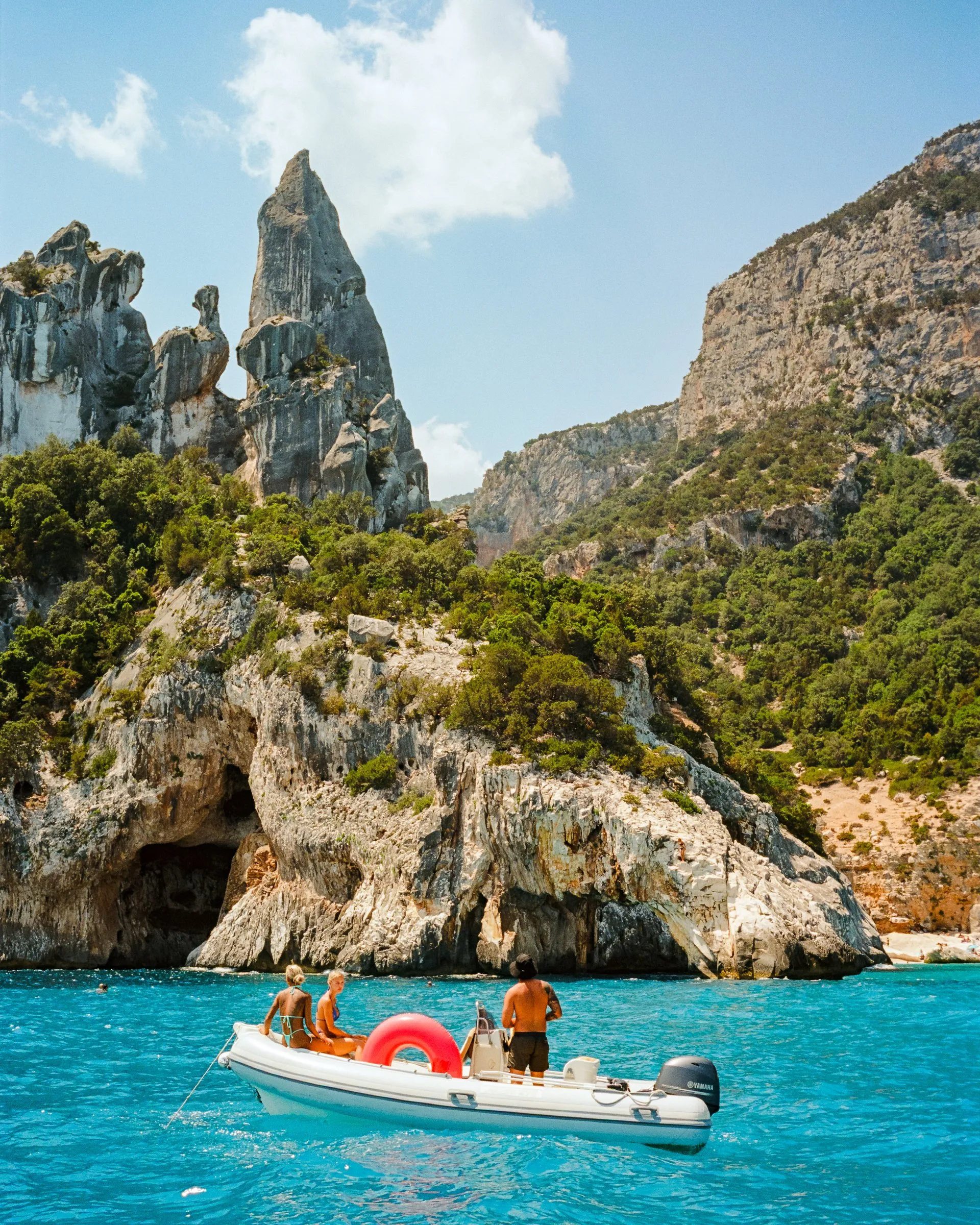 A dinghy floats in bright blue water below the limestone spire of Cala Goloritzé