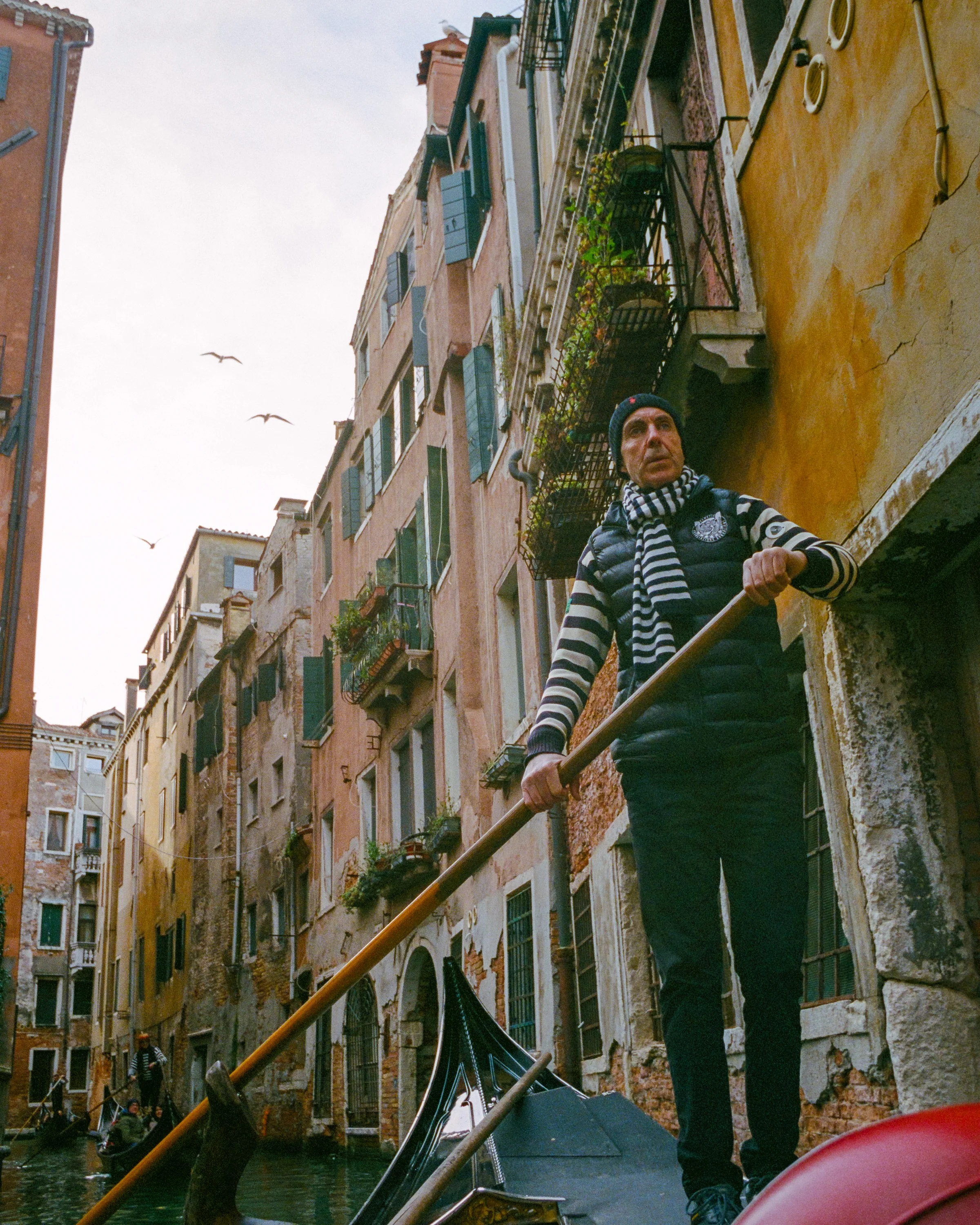A gondolier in a striped top rowing between tall houses
