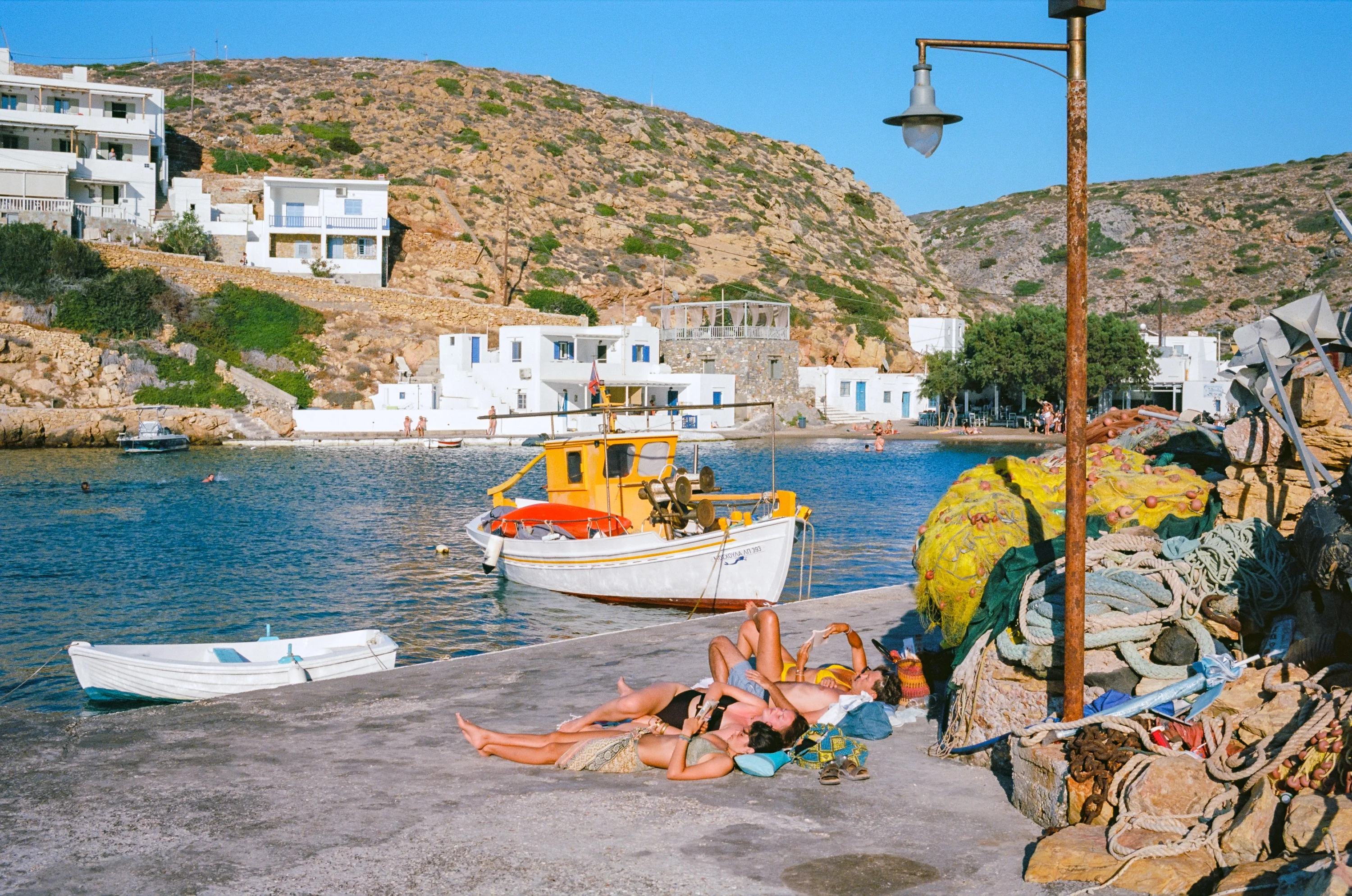 Small boats in a still harbour, nets and a lamp post on the quay, a village on the hill