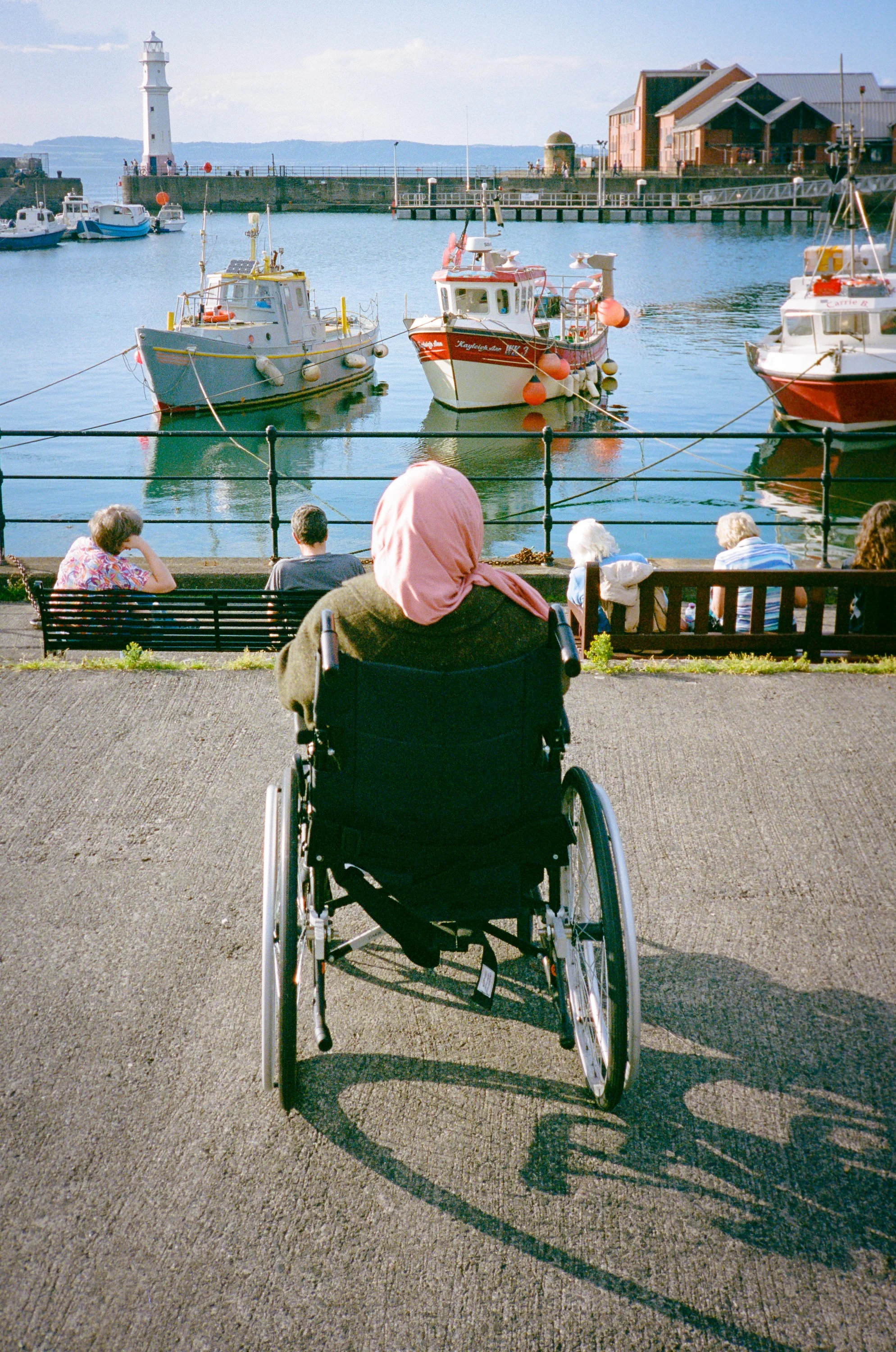 A woman in a wheelchair looking out over boats in Newhaven harbour
