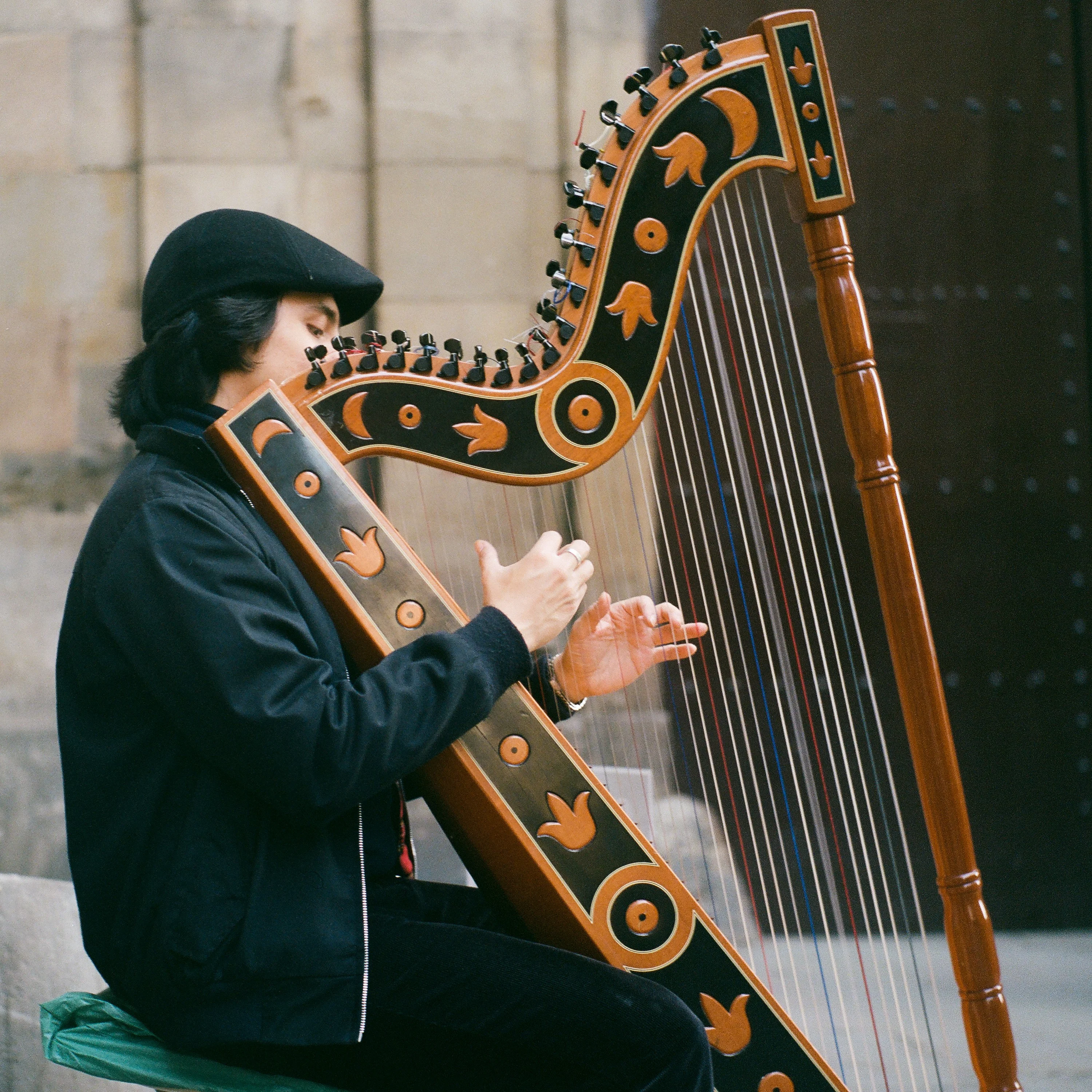 A street musician in a cap playing a painted harp