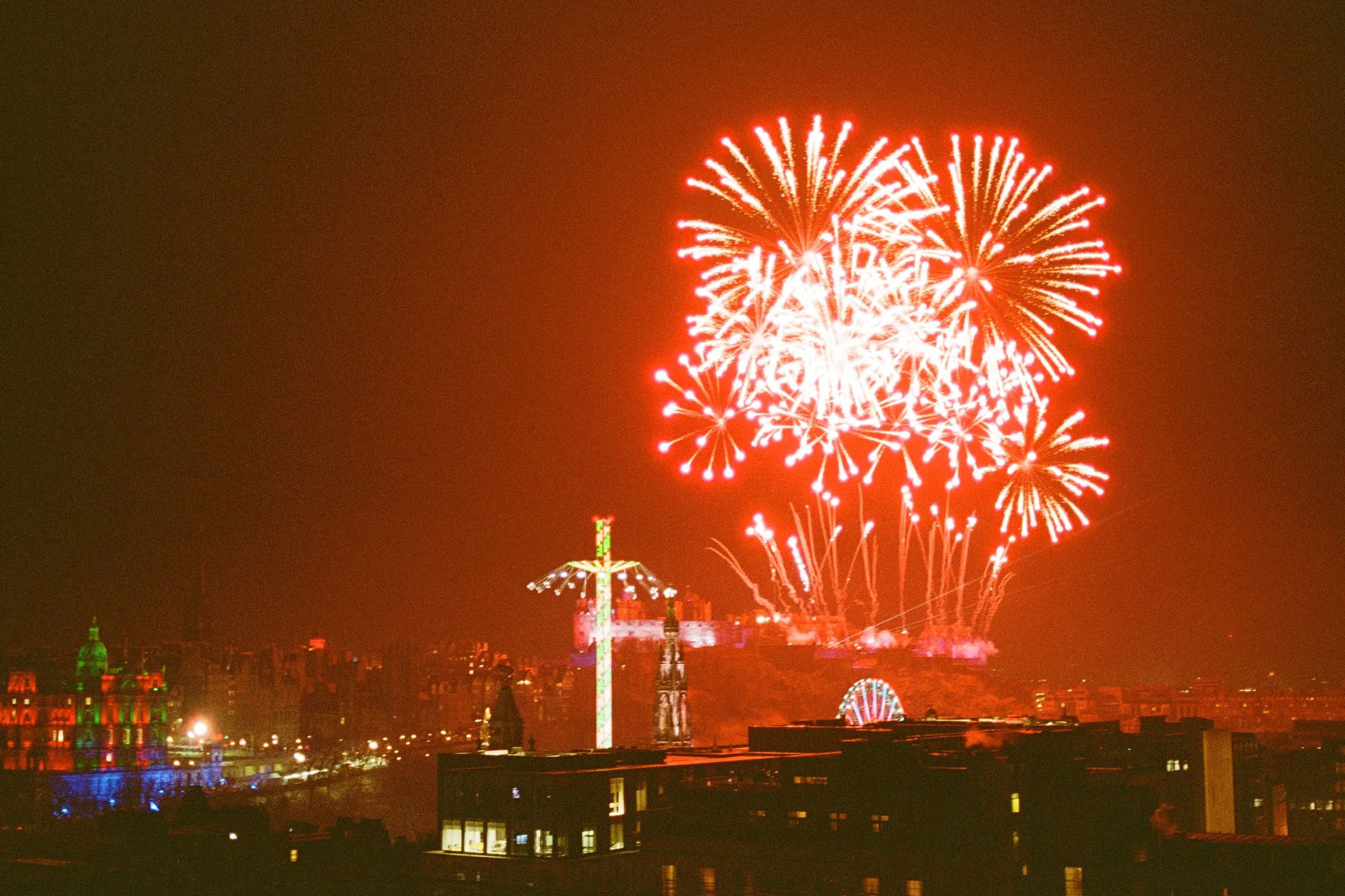Hogmanay fireworks bursting over Edinburgh Castle, the city glowing red below