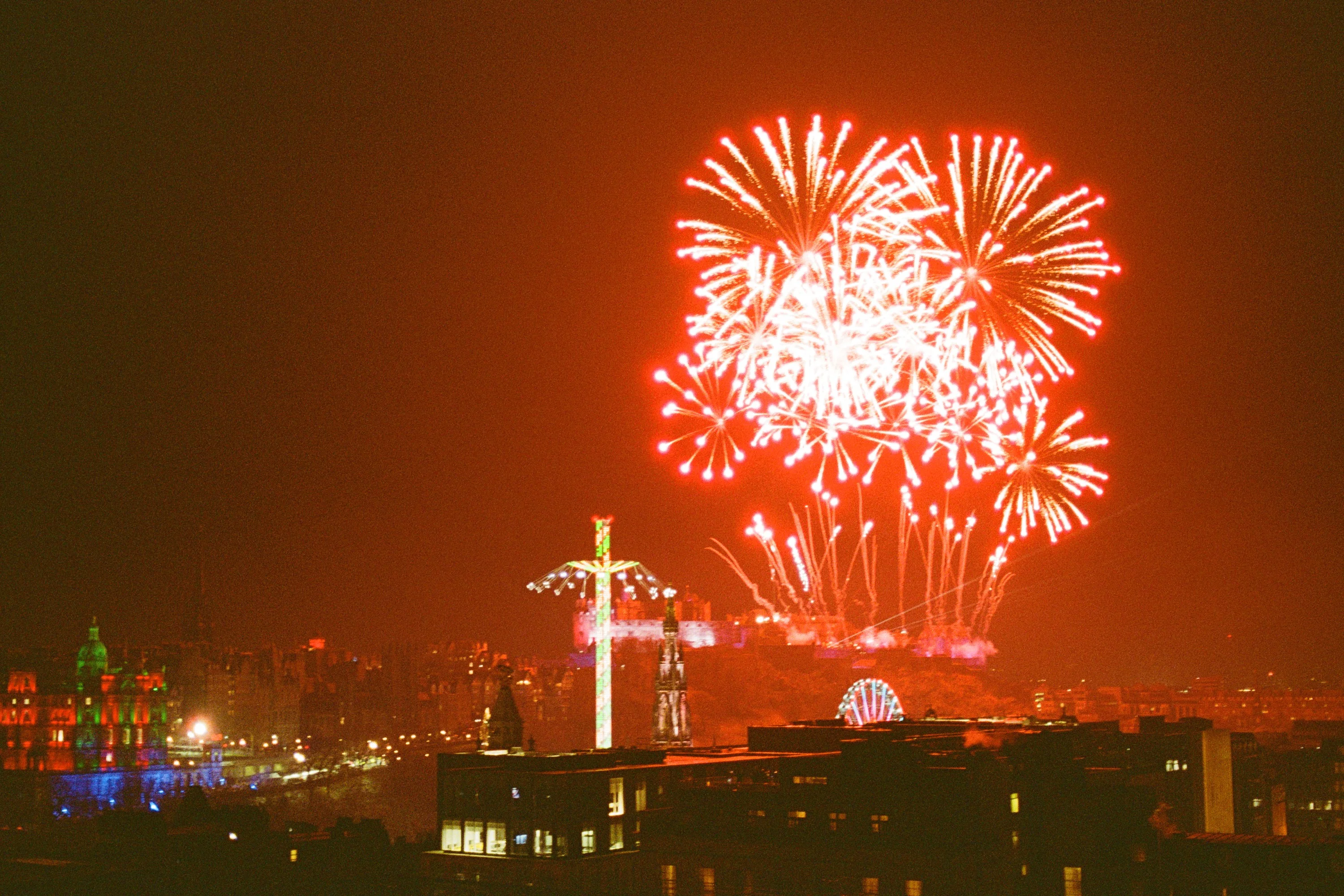 Hogmanay fireworks bursting over Edinburgh Castle, the city glowing red below