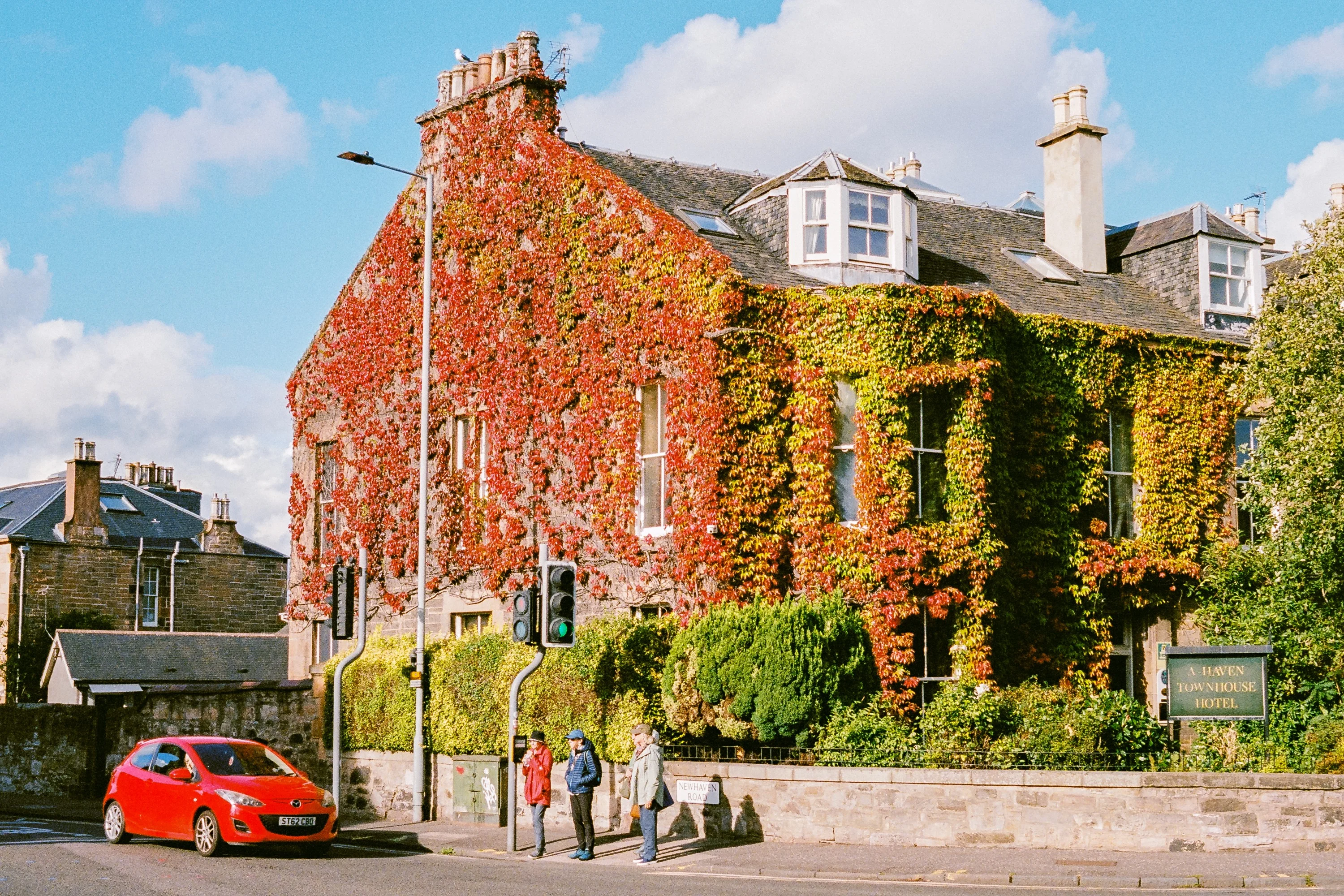 A house covered in red ivy, a red car parked outside