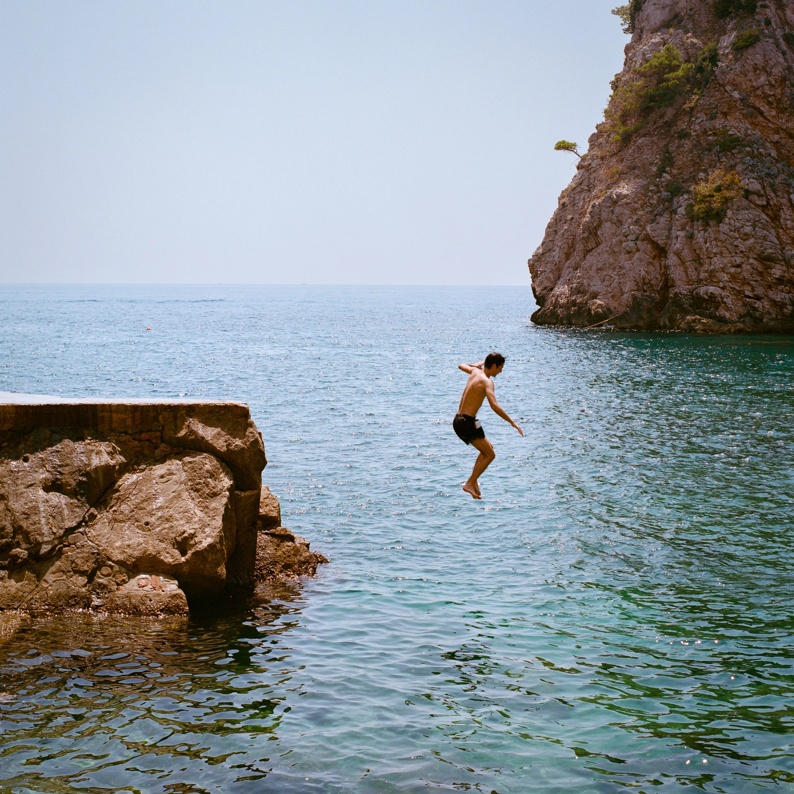 A man jumps from the rocks into the sea