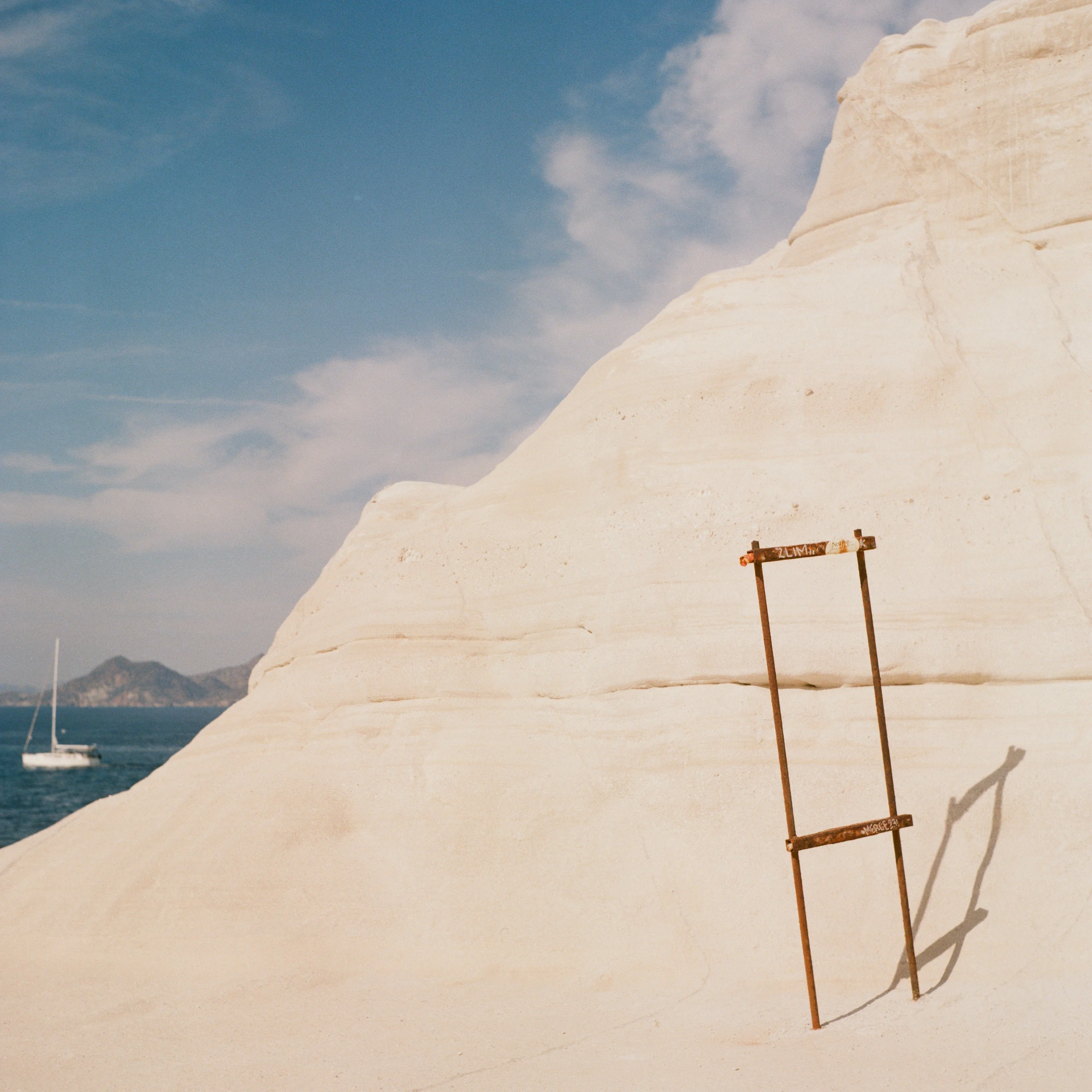A rusty ladder fixed to smooth white rock above the sea