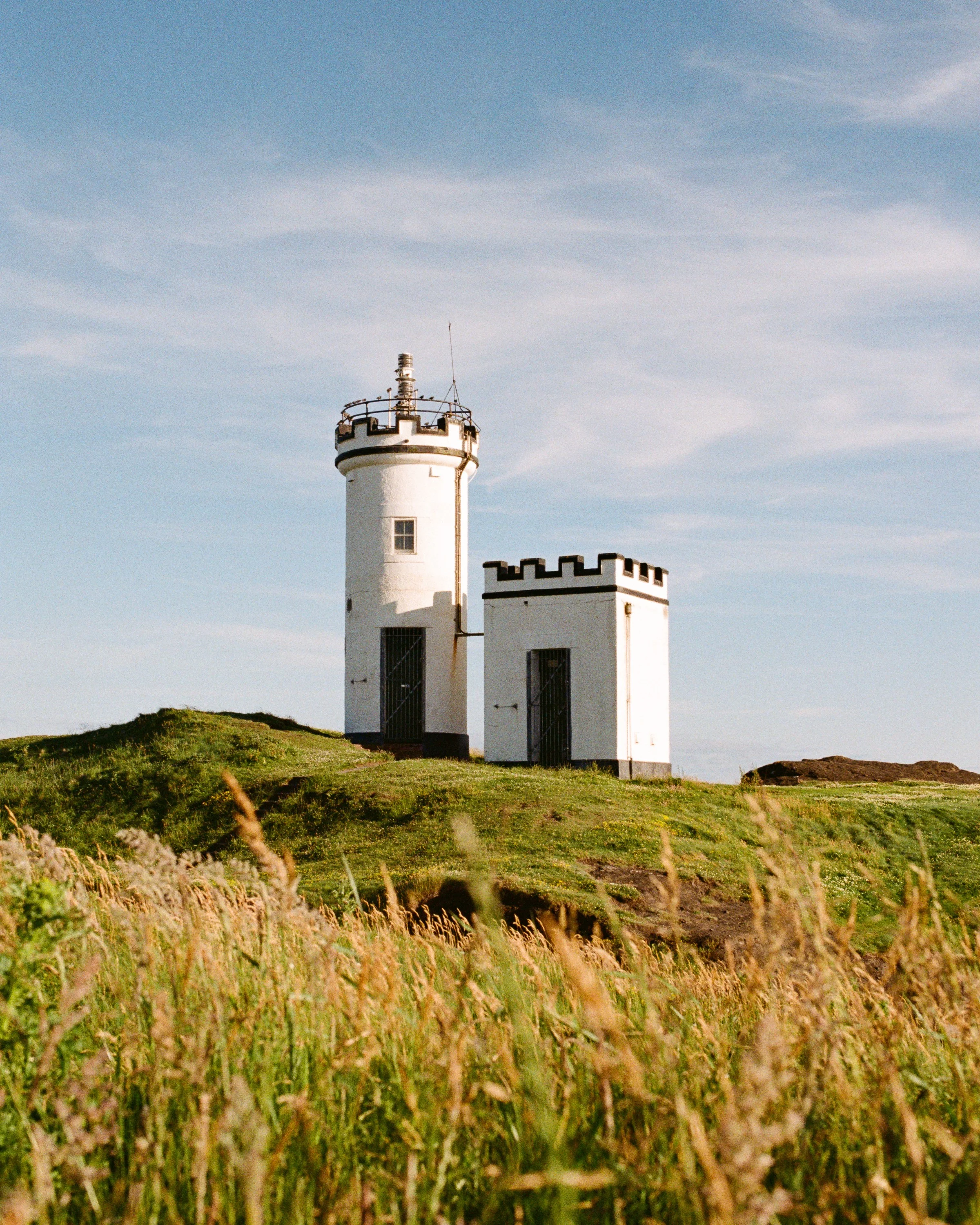 A small white tower on a grassy headland above long grass