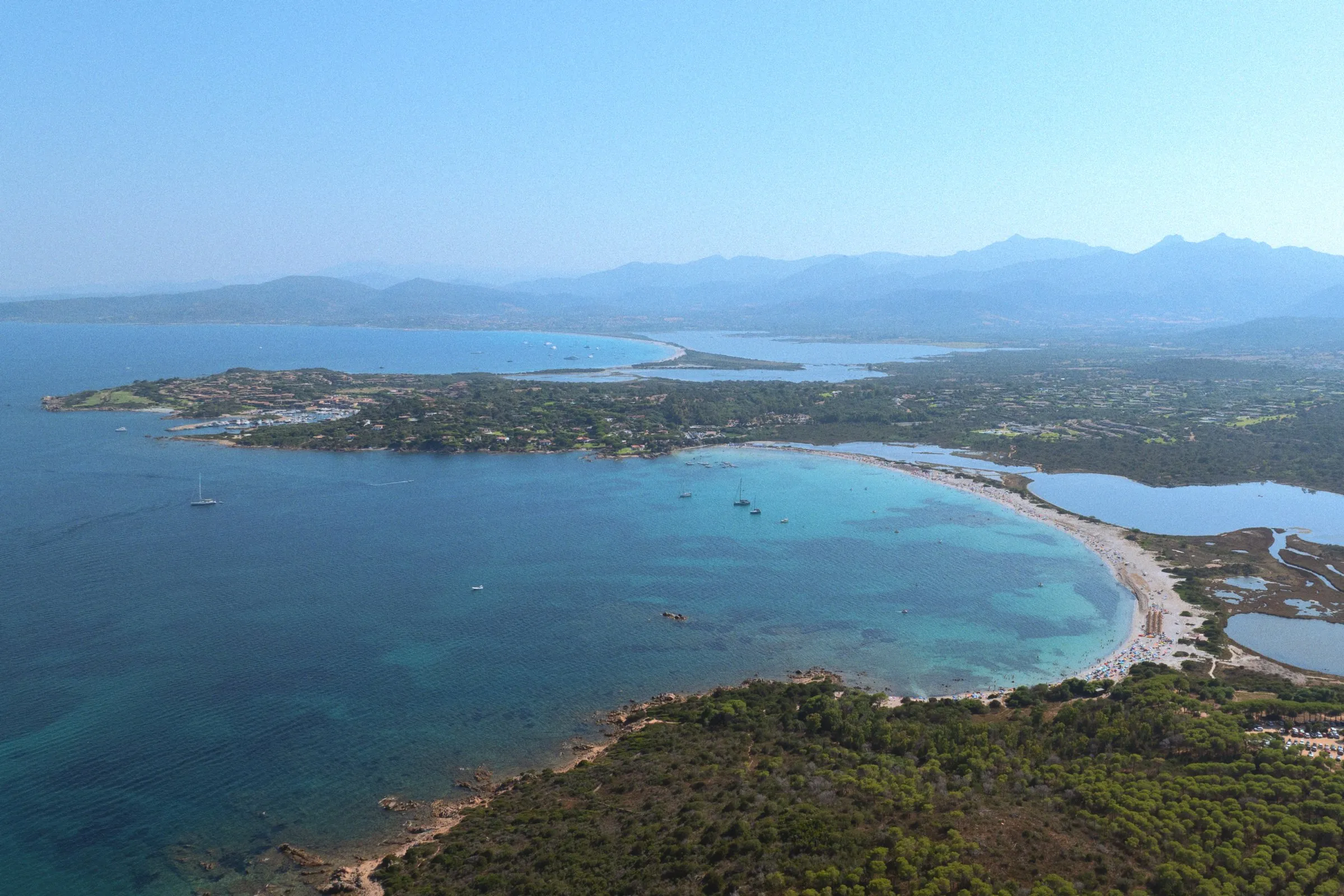 A wide aerial view of a bay, a lagoon and hazy mountains beyond