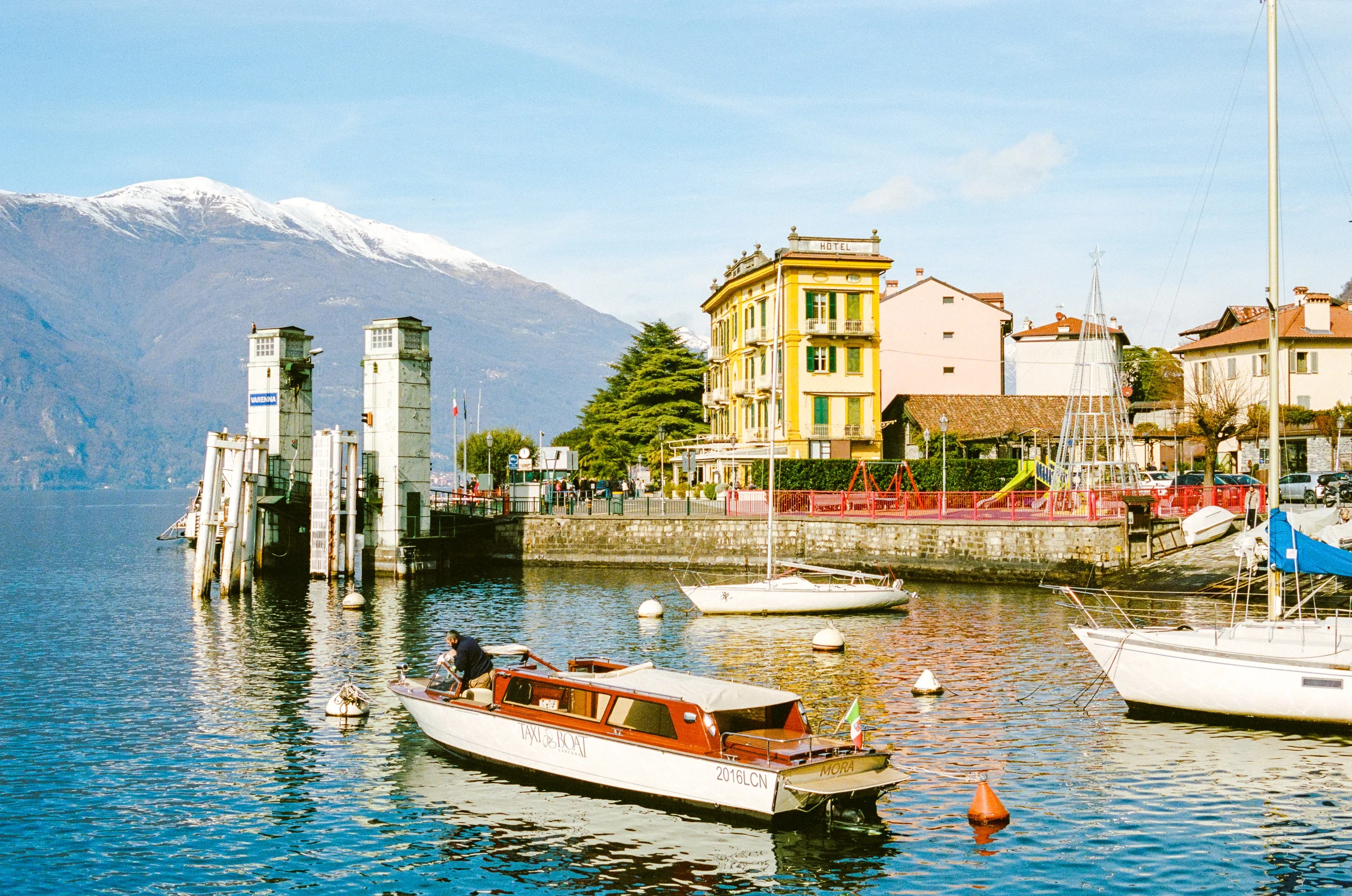 Wooden boats moored in a small harbour on Lake Como with snow-capped mountains behind