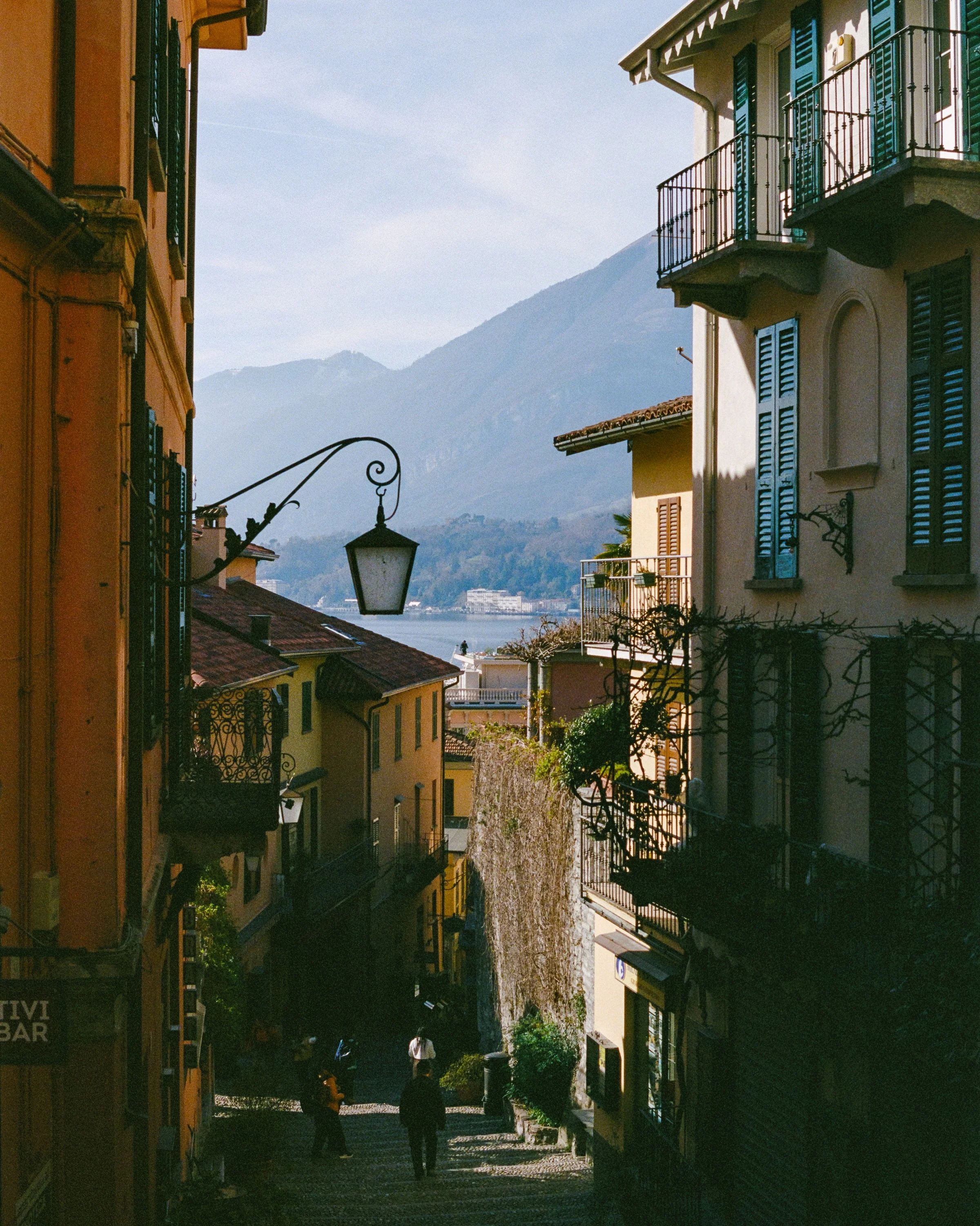 A narrow stepped lane between old houses leading down towards the lake and mountains