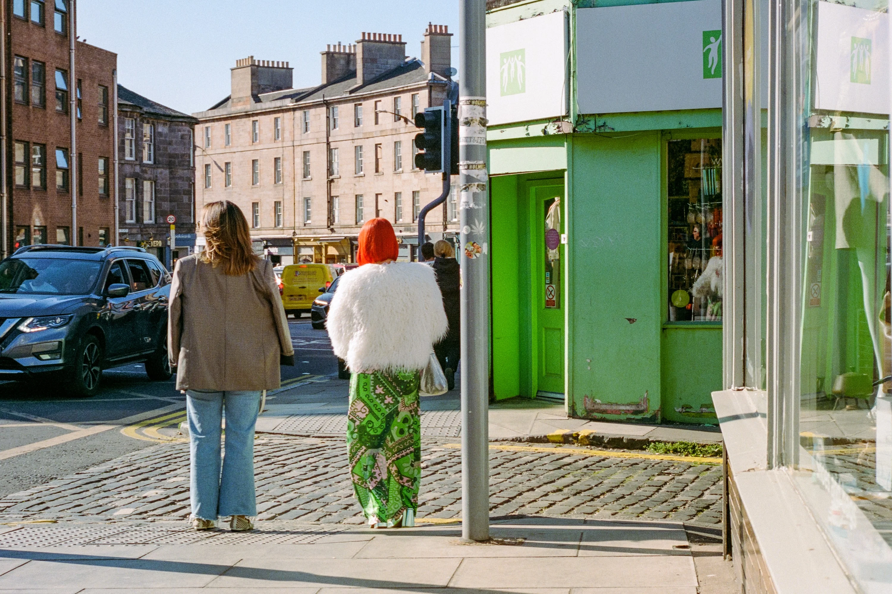 Two women waiting to cross a cobbled street, one with red hair