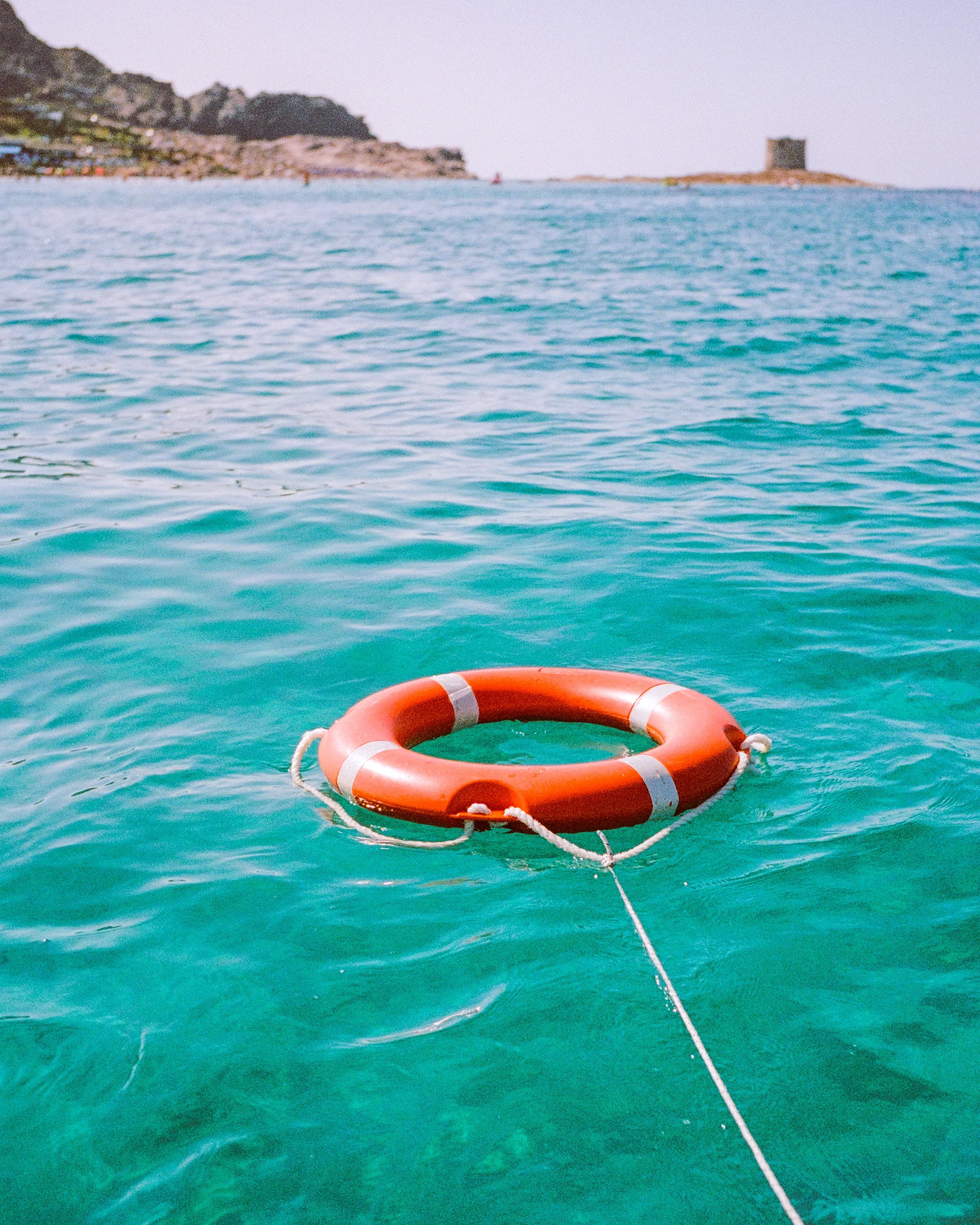 An orange lifebuoy floating on clear turquoise water, a watchtower on the horizon