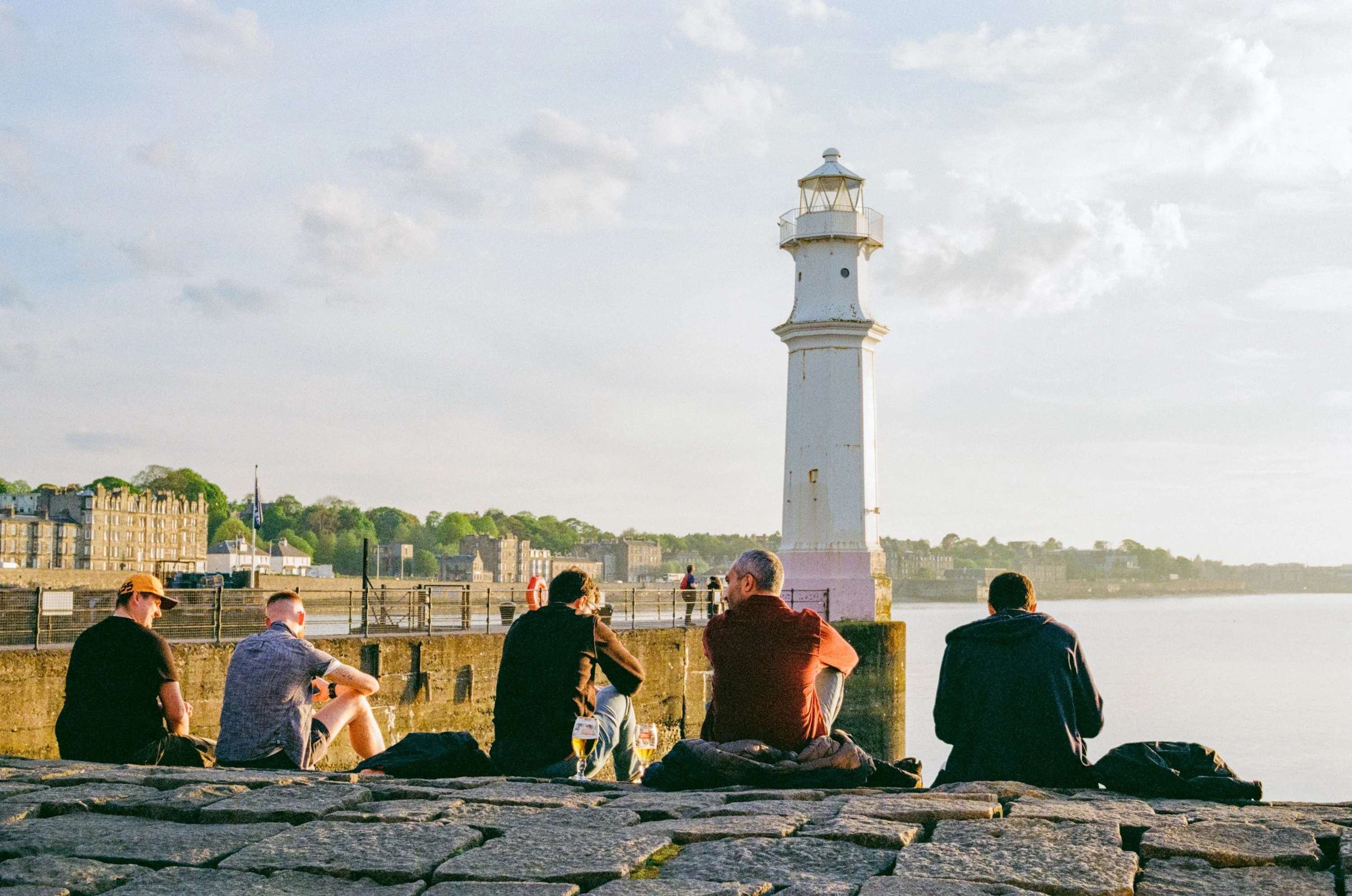 People sitting on the harbour wall in silhouette beside Newhaven lighthouse