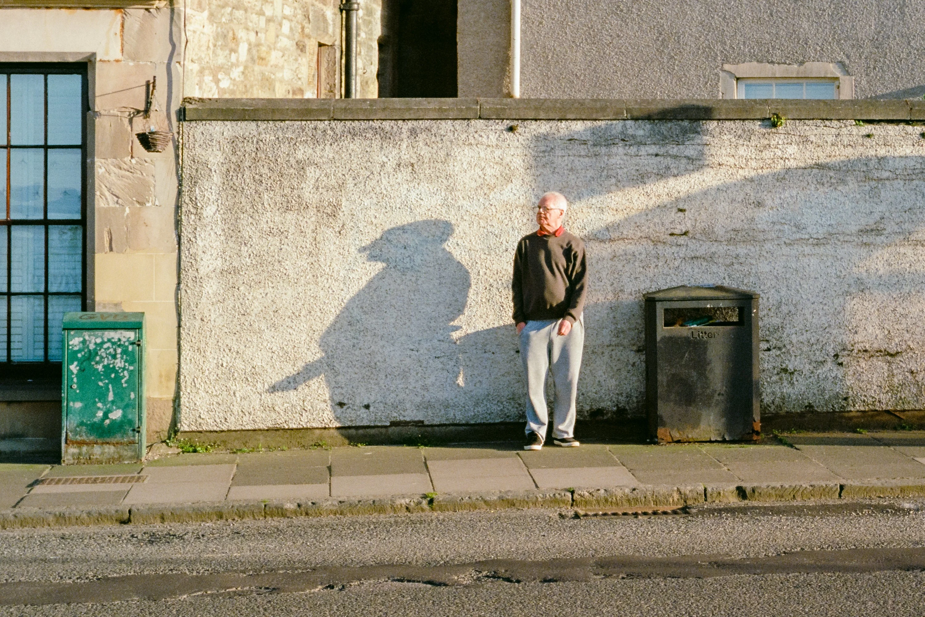 A man standing against a white wall beside his shadow