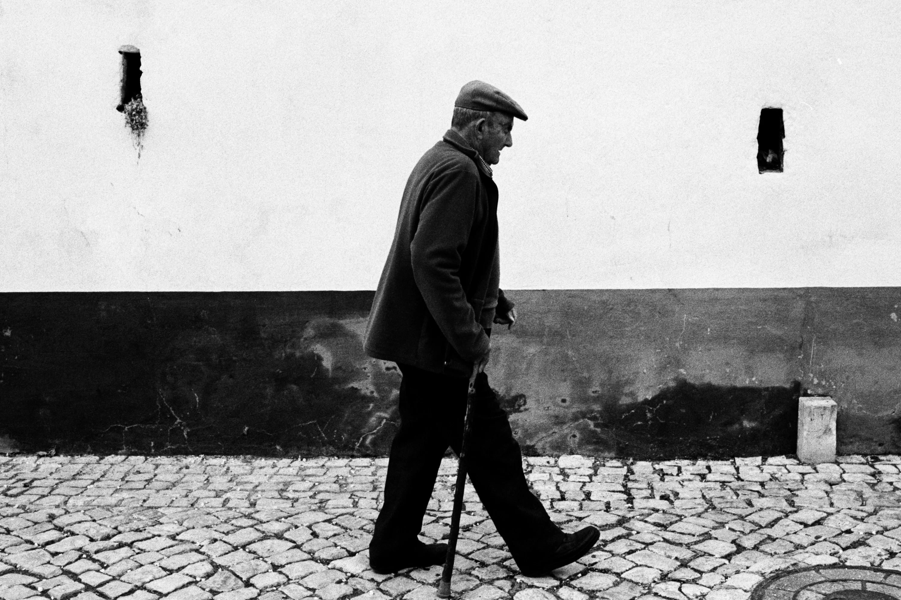 Black and white: a man with a cane walking along a white wall