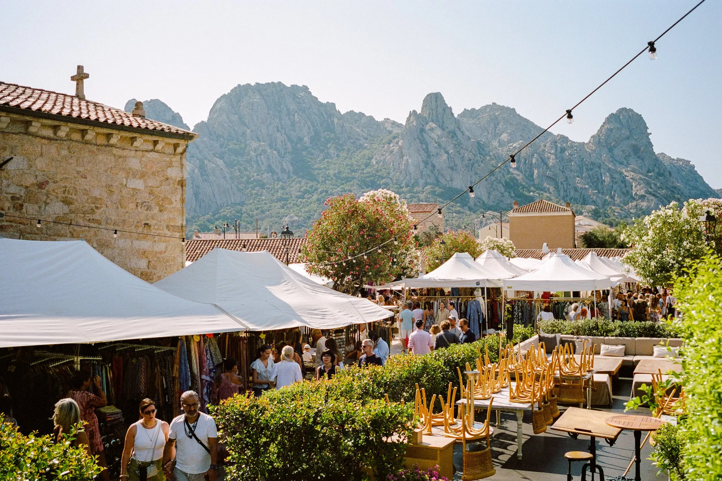 Market stalls and white umbrellas filling a village square below granite peaks