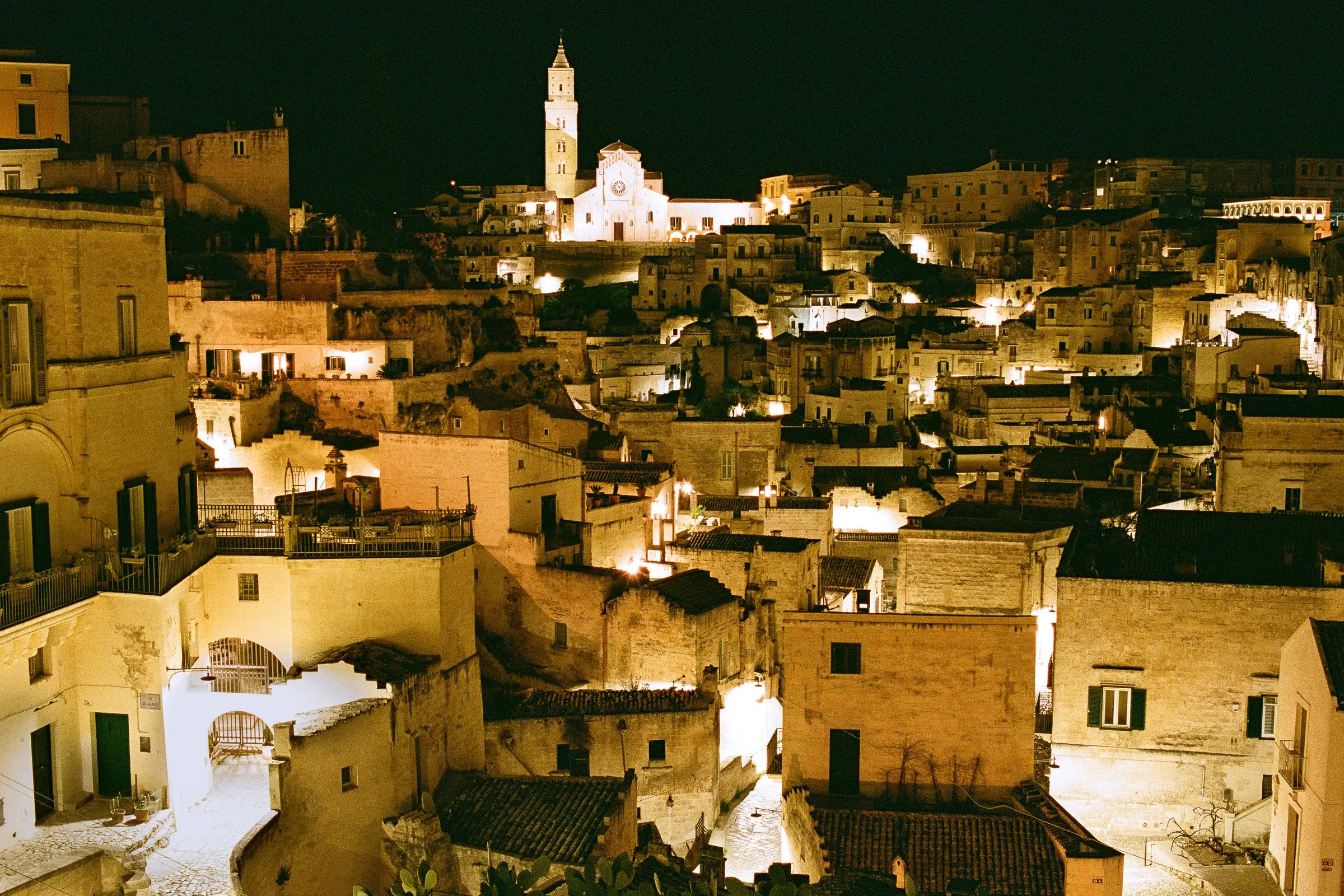 Matera's stone houses lit at night below the floodlit cathedral