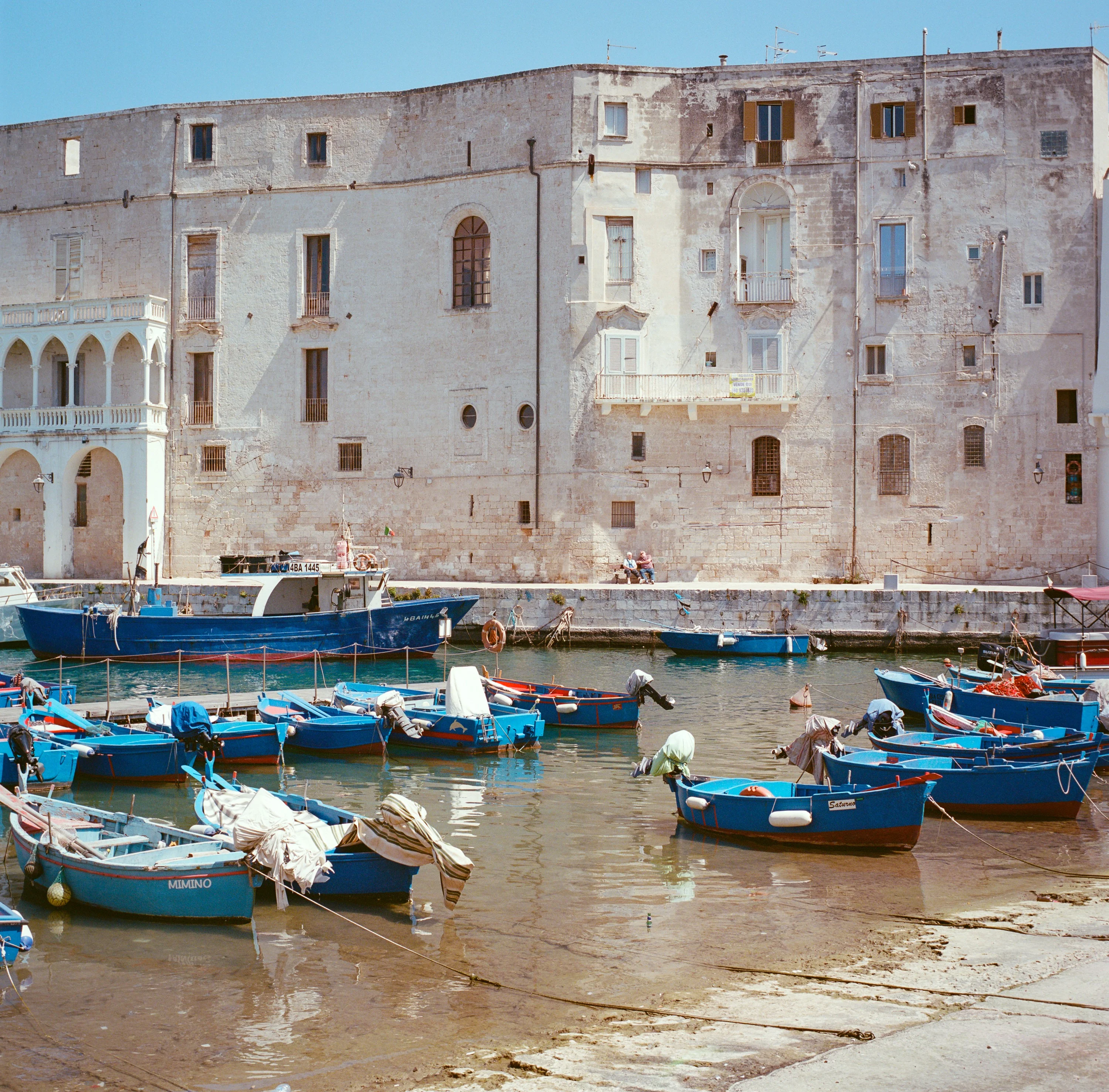Blue fishing boats in the old harbour at Monopoli below weathered stone walls