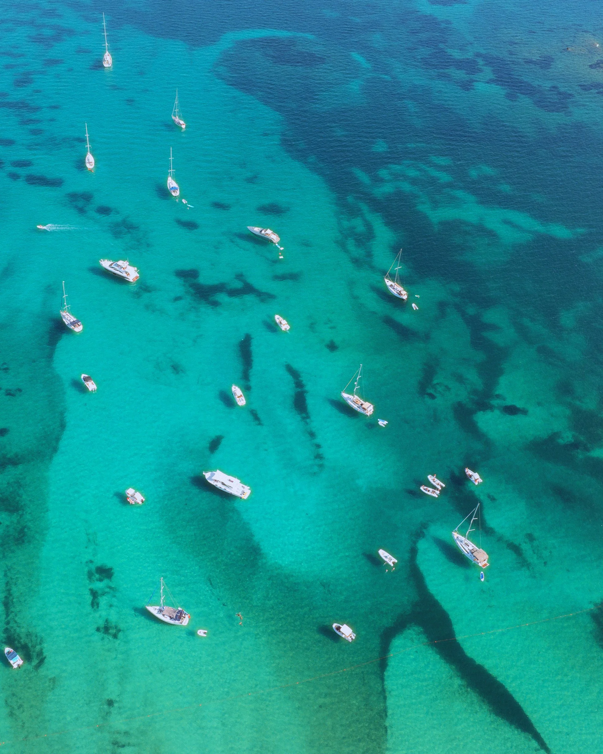 Boats seen from directly above, scattered over turquoise water and dark seagrass